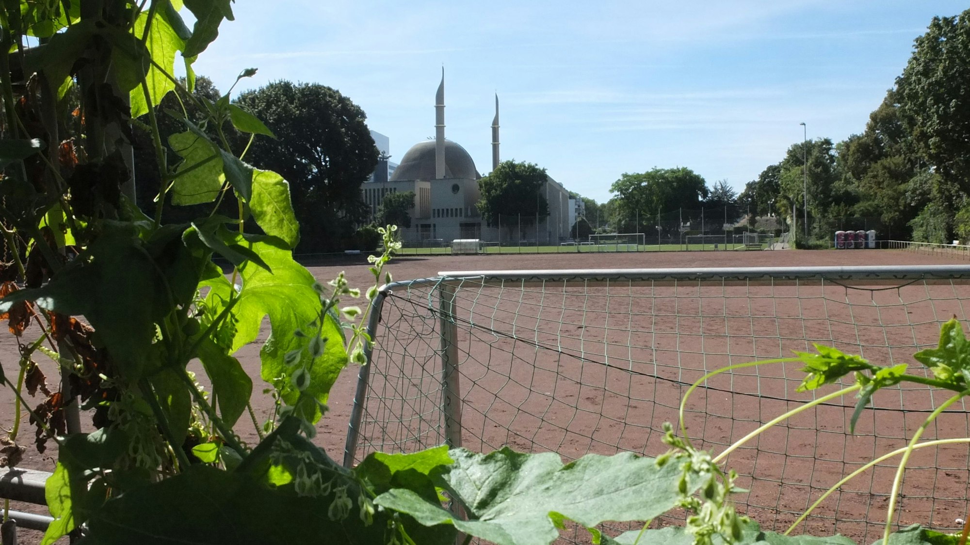 Ein großer Ascheplatz ist zu sehen, im Hintergrund die Moschee Ehrenfeld.