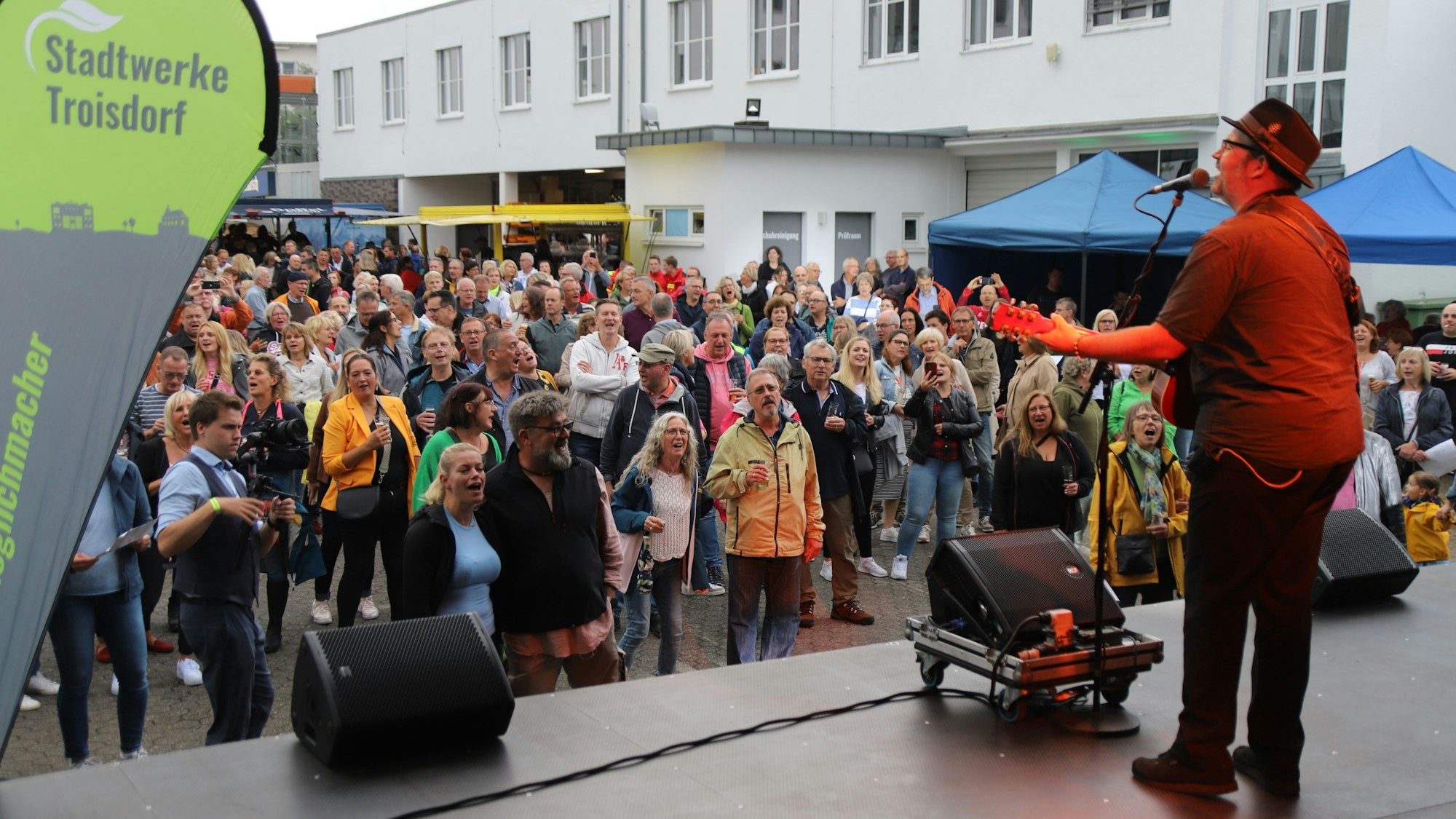 Der Sänger Björn Heuser steht mit Gitarre auf einer Bühne, vor der die Zuschauer begeistert mitsingen.