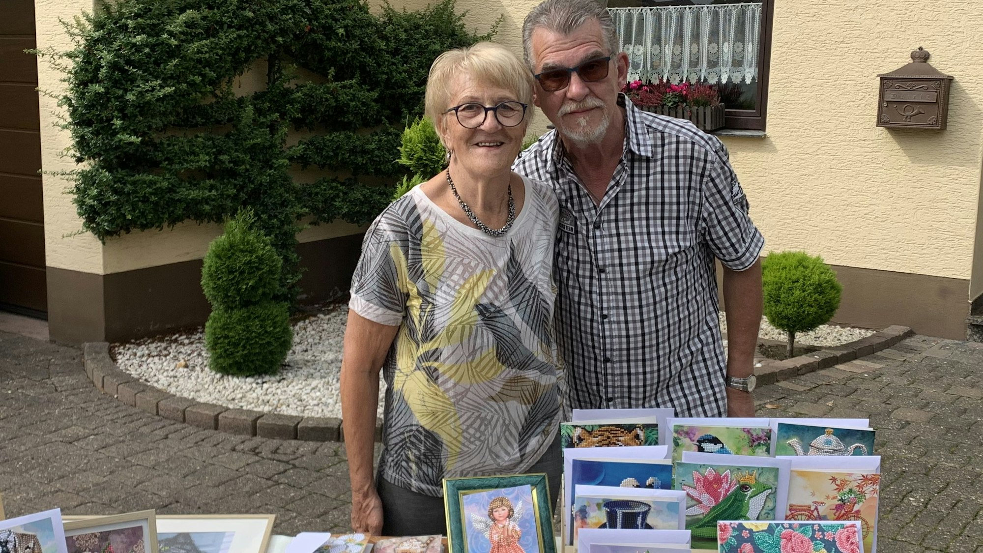 Das Bild zeigt die Künstlerin und ihren Mann am Stad mit den bunten Grußkarten.