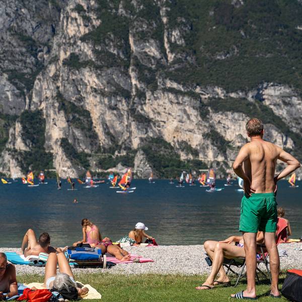 Urlauber liegen und stehen an einem Strand am italienischen Gardasee.