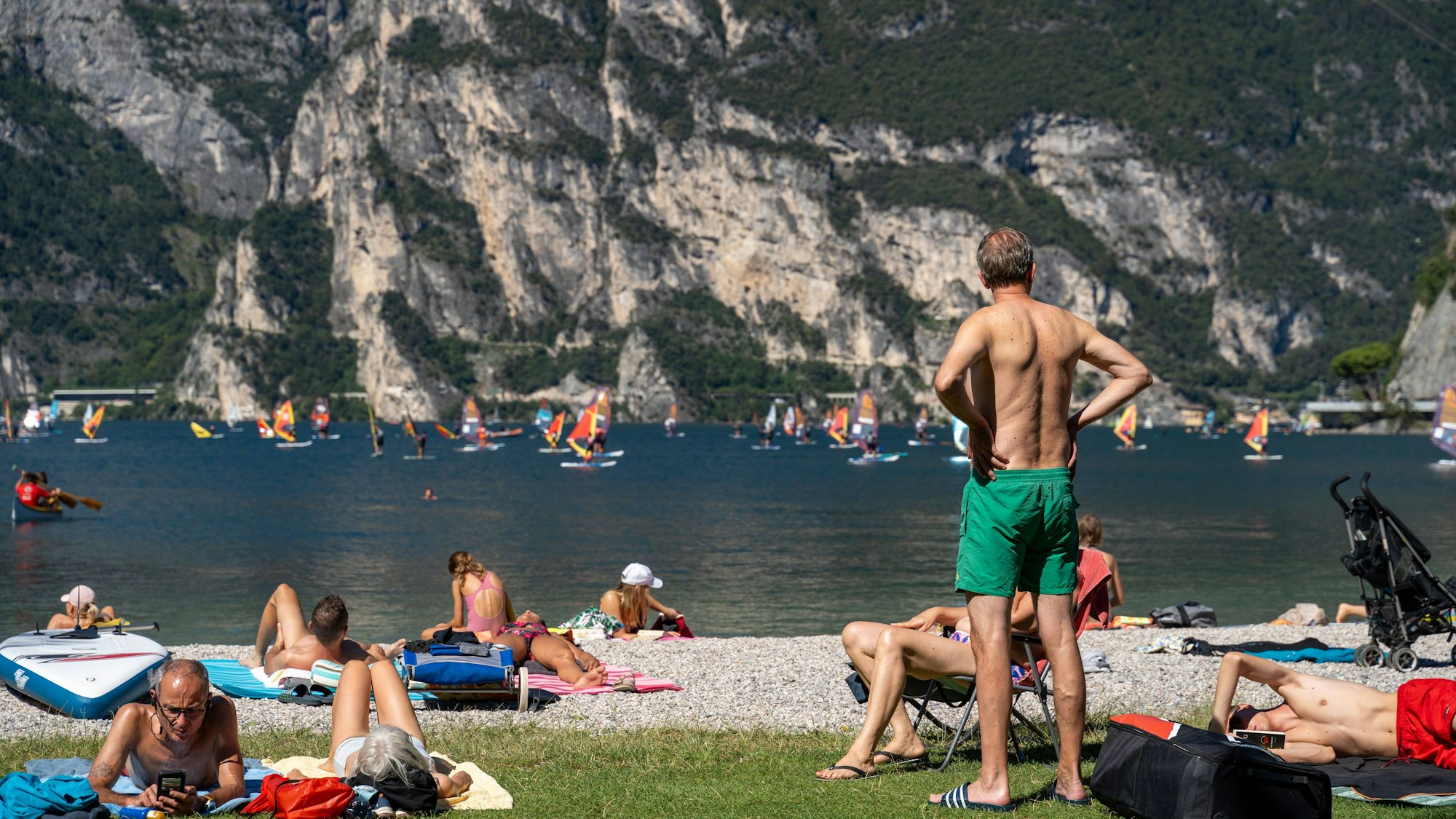 Urlauber liegen und stehen an einem Strand am italienischen Gardasee.