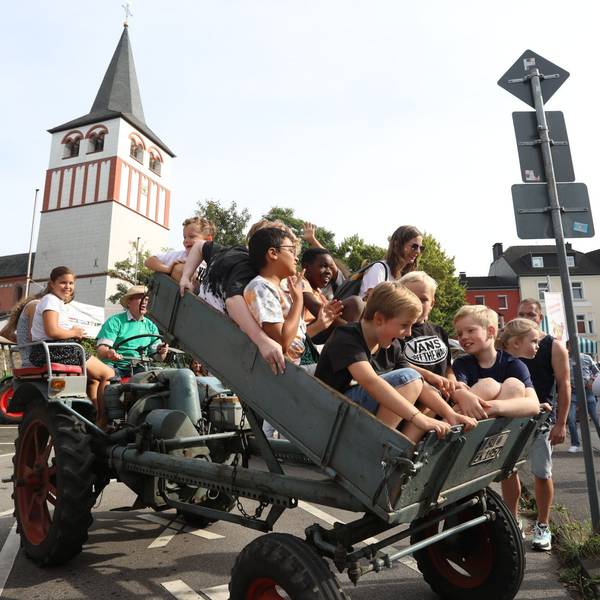 Lachende Kinder sitzen in einem Kipphänger vor einem Traktor, der soeben aufgestellt wird.