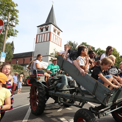 Lachende Kinder sitzen in einem Kipphänger vor einem Traktor, der soeben aufgestellt wird.