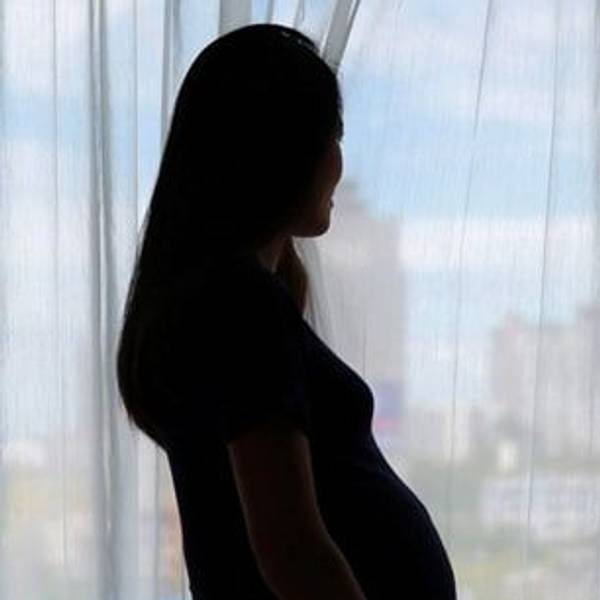 Eine schwangere Frau steht im Gegenlicht. Es ist nur die Silhouette zu sehen.