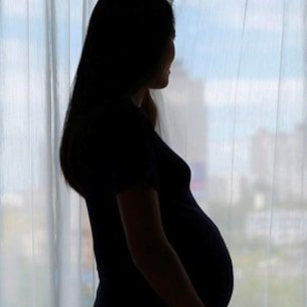 Eine schwangere Frau steht im Gegenlicht. Es ist nur die Silhouette zu sehen.