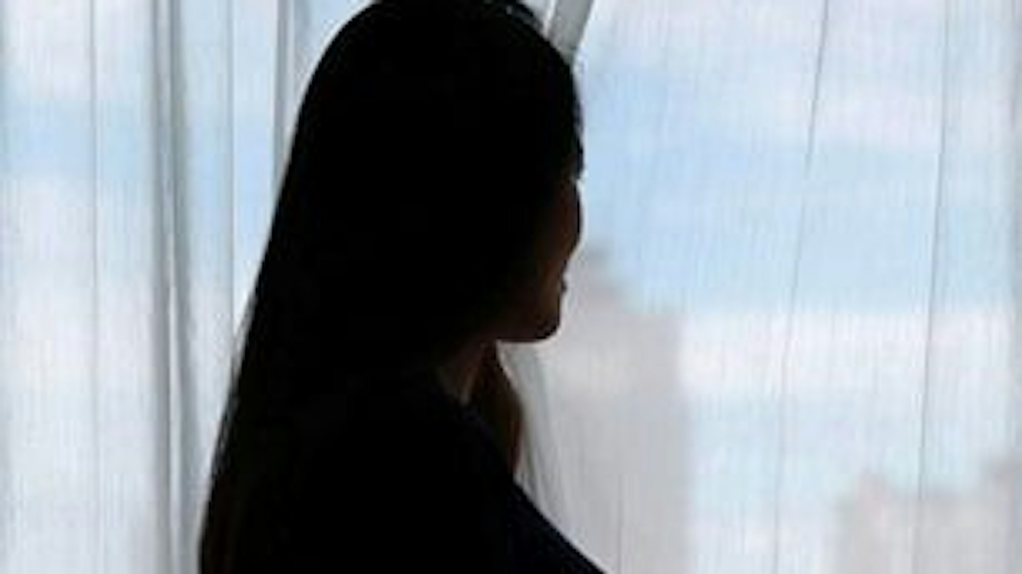 Eine schwangere Frau steht im Gegenlicht. Es ist nur die Silhouette zu sehen.