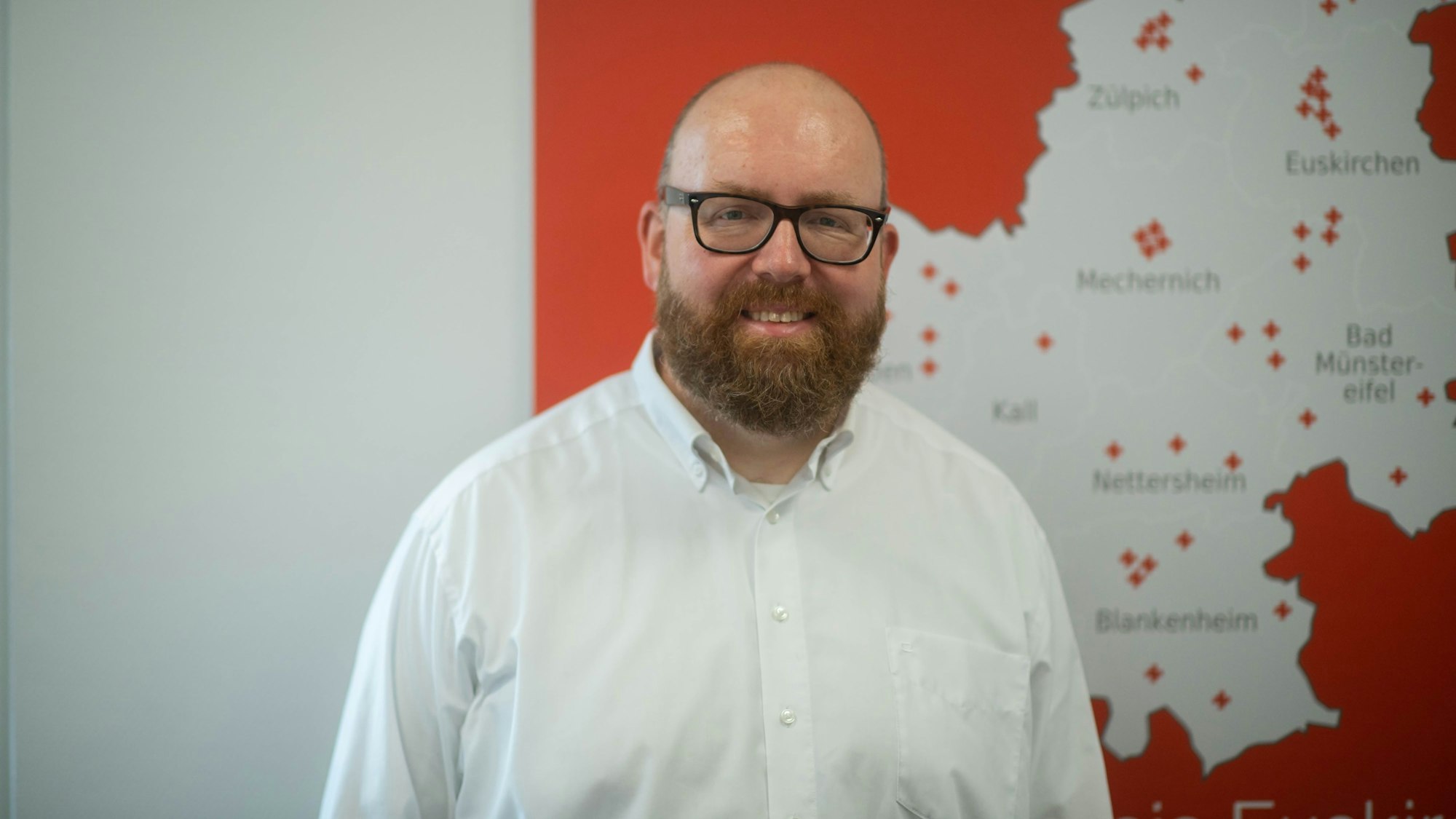 Boris Brandhoff ist Chef der Integrationsagentur des Deutschen Roten Kreuzes im Kreis Euskirchen. Er steht vor einer Karte des Kreises Euskirchen.