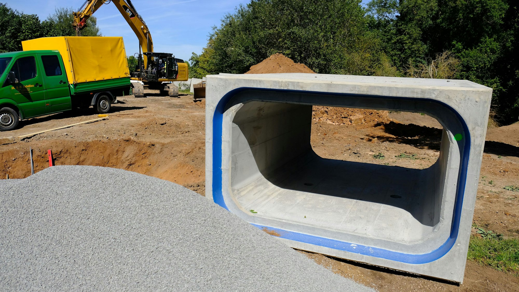 An einer Baustelle in Satzvey liegt ein kastenförmiges Betonrohr, das zum Hochwasserschutz eingesetzt wird. Im Hintergrund sind ein Bagger und ein Lkw zu sehen.