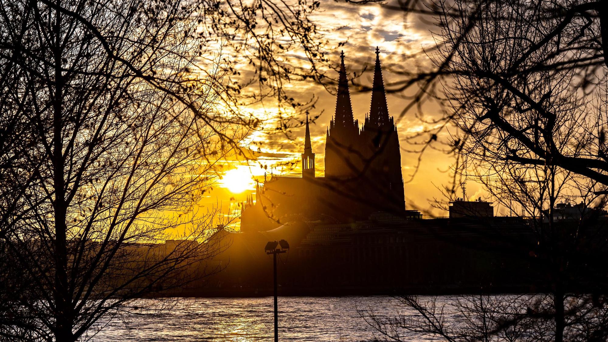 Die Silhouette des Kölner Doms ist im Sonnenuntergang von der gegenüberliegenden Seite des Rheins zu sehen.