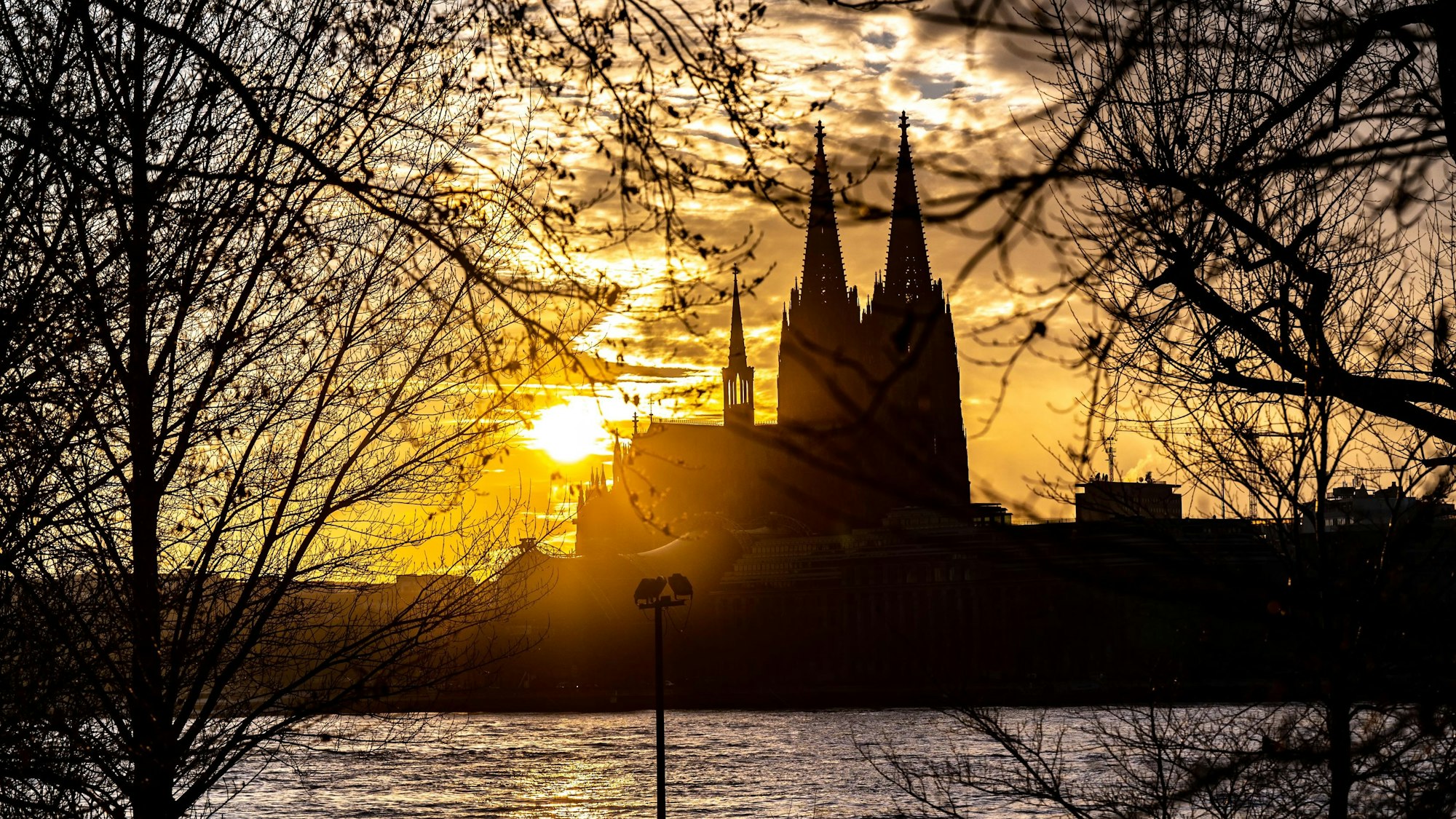 Die Silhouette des Kölner Doms ist im Sonnenuntergang von der gegenüberliegenden Seite des Rheins zu sehen.