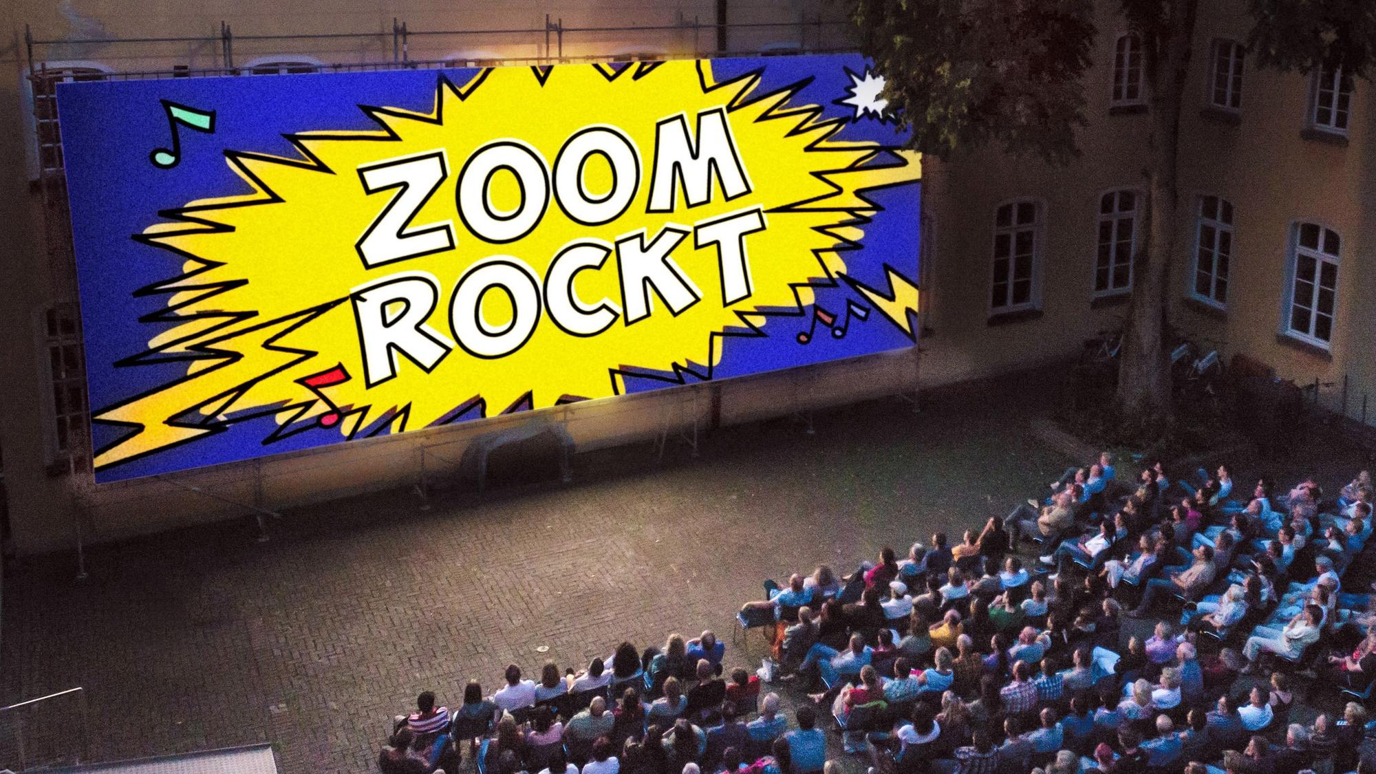Das Publikum schaut auf ein Plakat mit der Aufschrift Zoom Rockt.