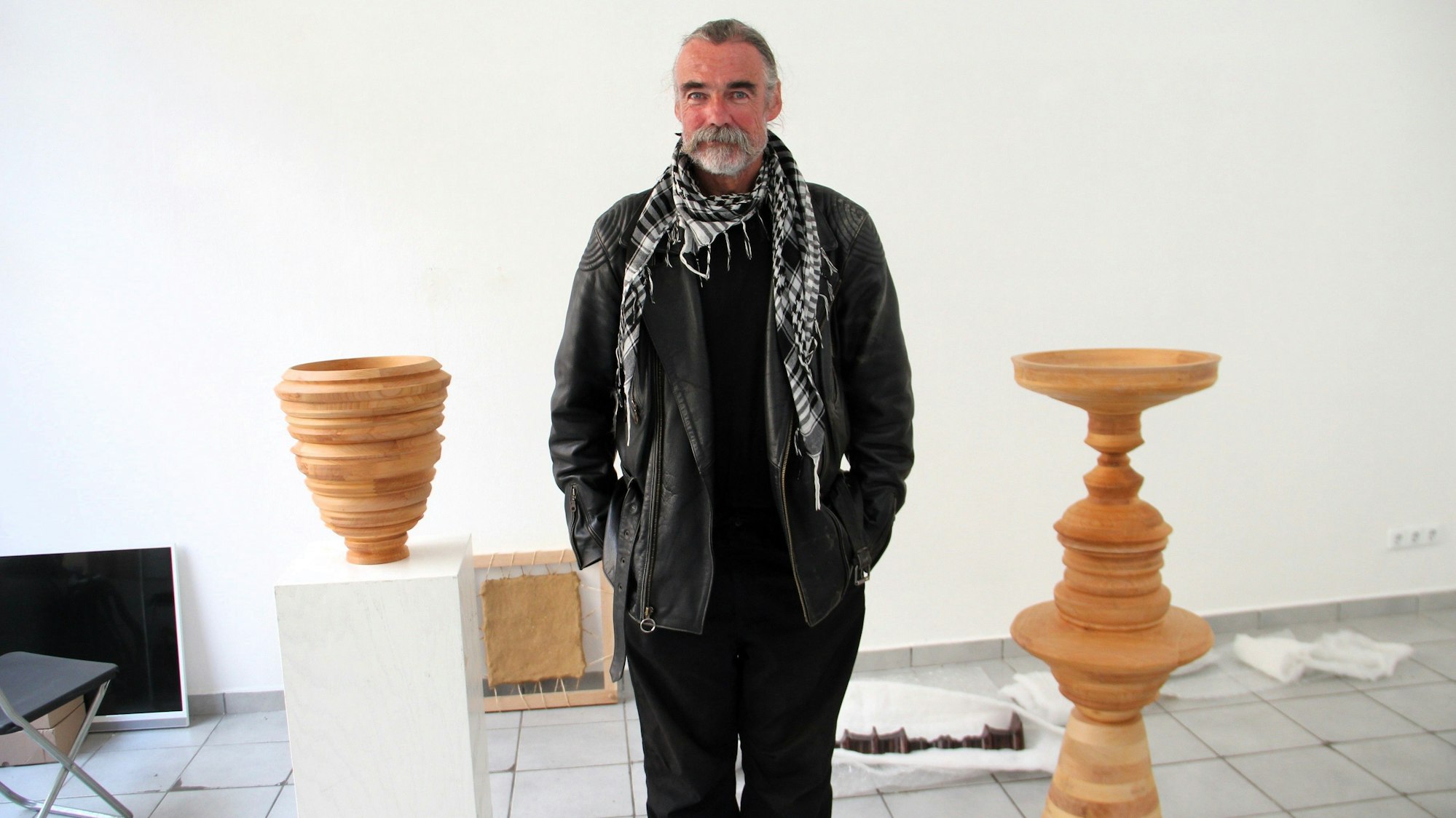 Ein Mann mit grauem Bart stehen zwischen Skulpturen in einem Raum.