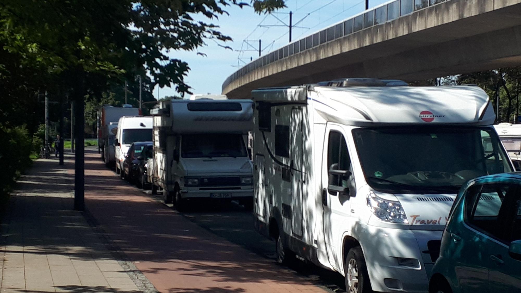 Mehrere Wohnmobile parken hintereinander an einer Straße.