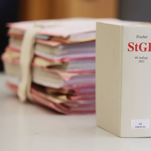 Gerichtsakten und Bücher zu Strafgesetzbuch und Strafprozessordnung liegen bzw. stehen liegen auf einem Tisch in einem Gerichtssaal.