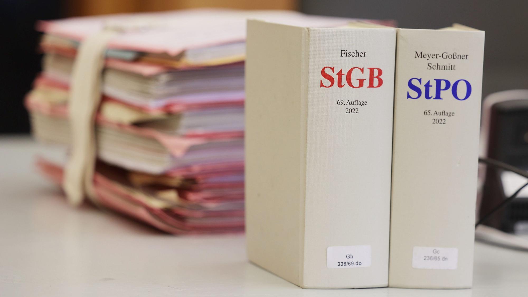 Gerichtsakten und Bücher zu Strafgesetzbuch und Strafprozessordnung liegen bzw. stehen liegen auf einem Tisch in einem Gerichtssaal.