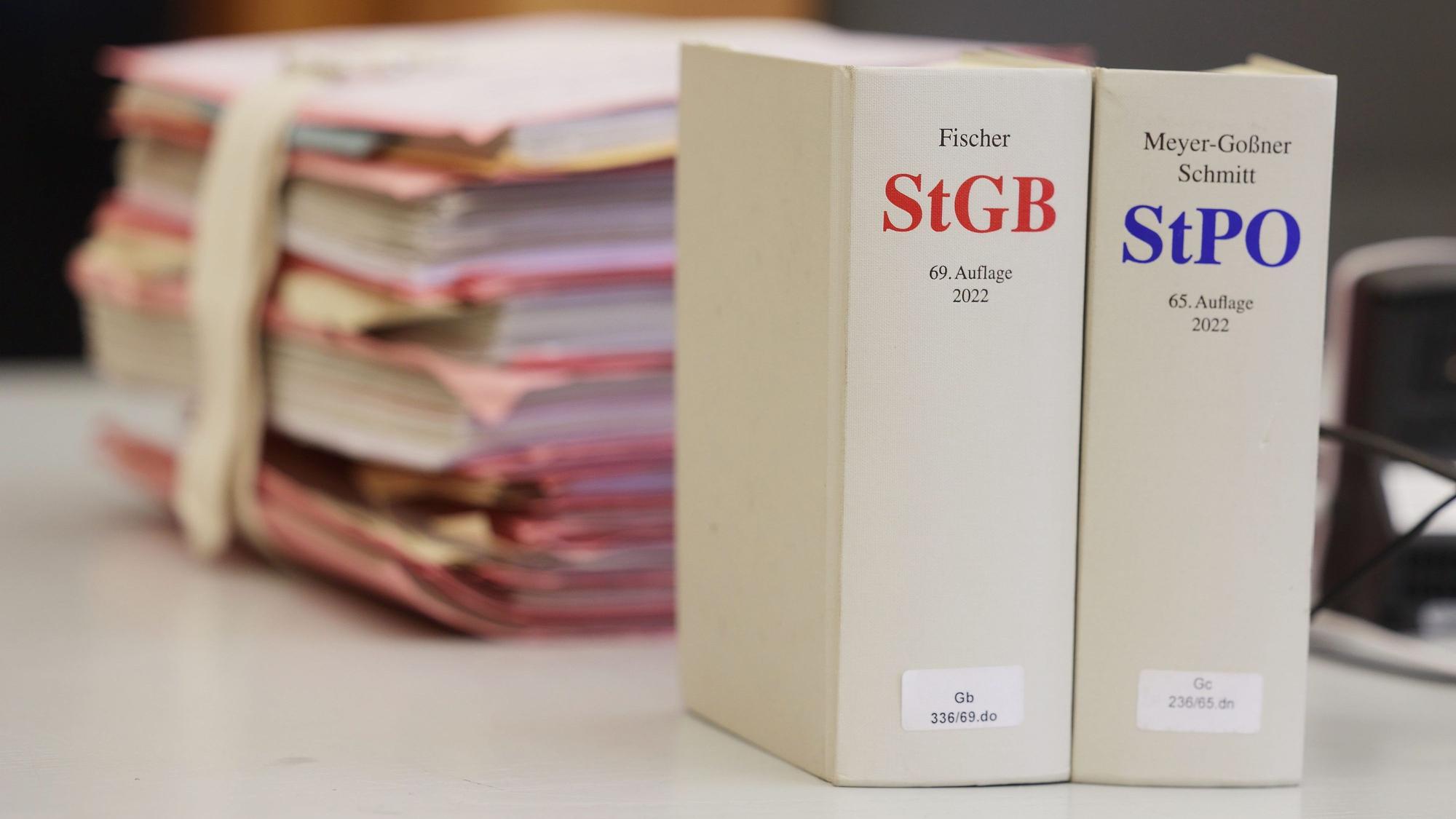 Gerichtsakten und Bücher zu Strafgesetzbuch und Strafprozessordnung liegen bzw. stehen liegen auf einem Tisch in einem Gerichtssaal.