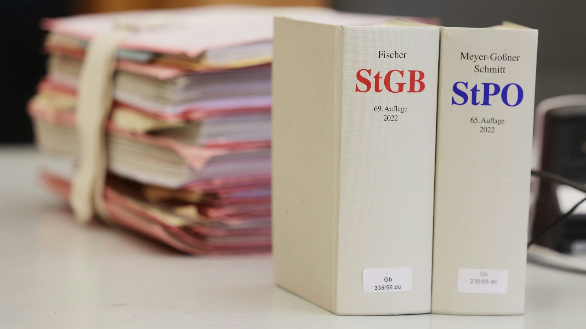 Gerichtsakten und Bücher zu Strafgesetzbuch und Strafprozessordnung liegen bzw. stehen liegen auf einem Tisch in einem Gerichtssaal.