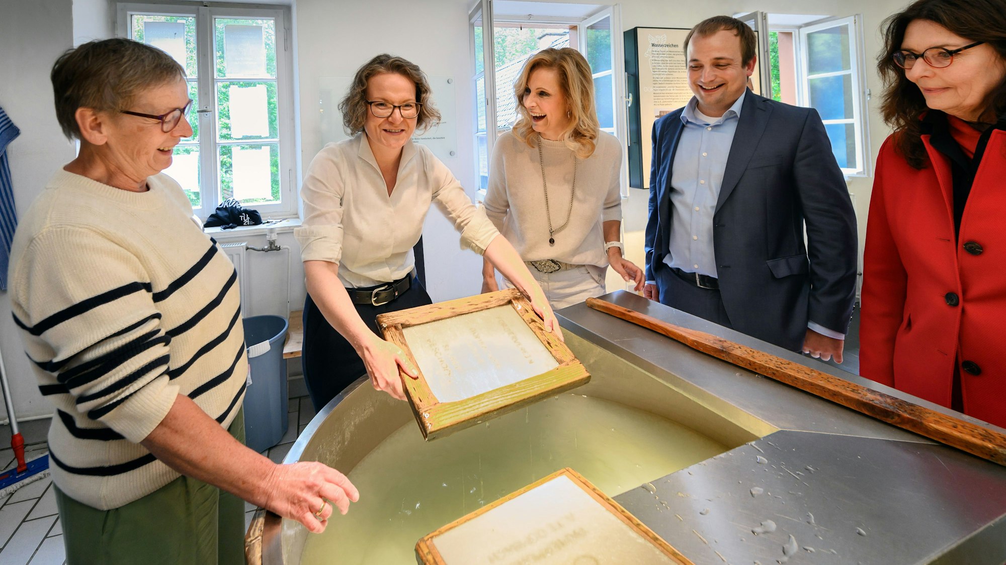 Mehrere Frauen und ein Mann stehen um den Papierschöpfbottich im LVR-Industriemuseum Papiermühle Alte Dombach in Bergisch Gladbach.
