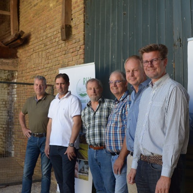 Sechs Landwirte stehen nebeneinander vor einem Scheunentor.