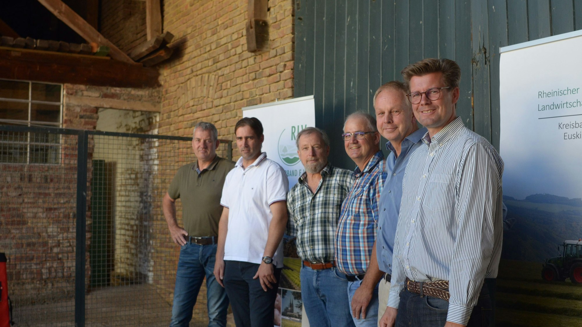 Sechs Landwirte stehen nebeneinander vor einem Scheunentor.