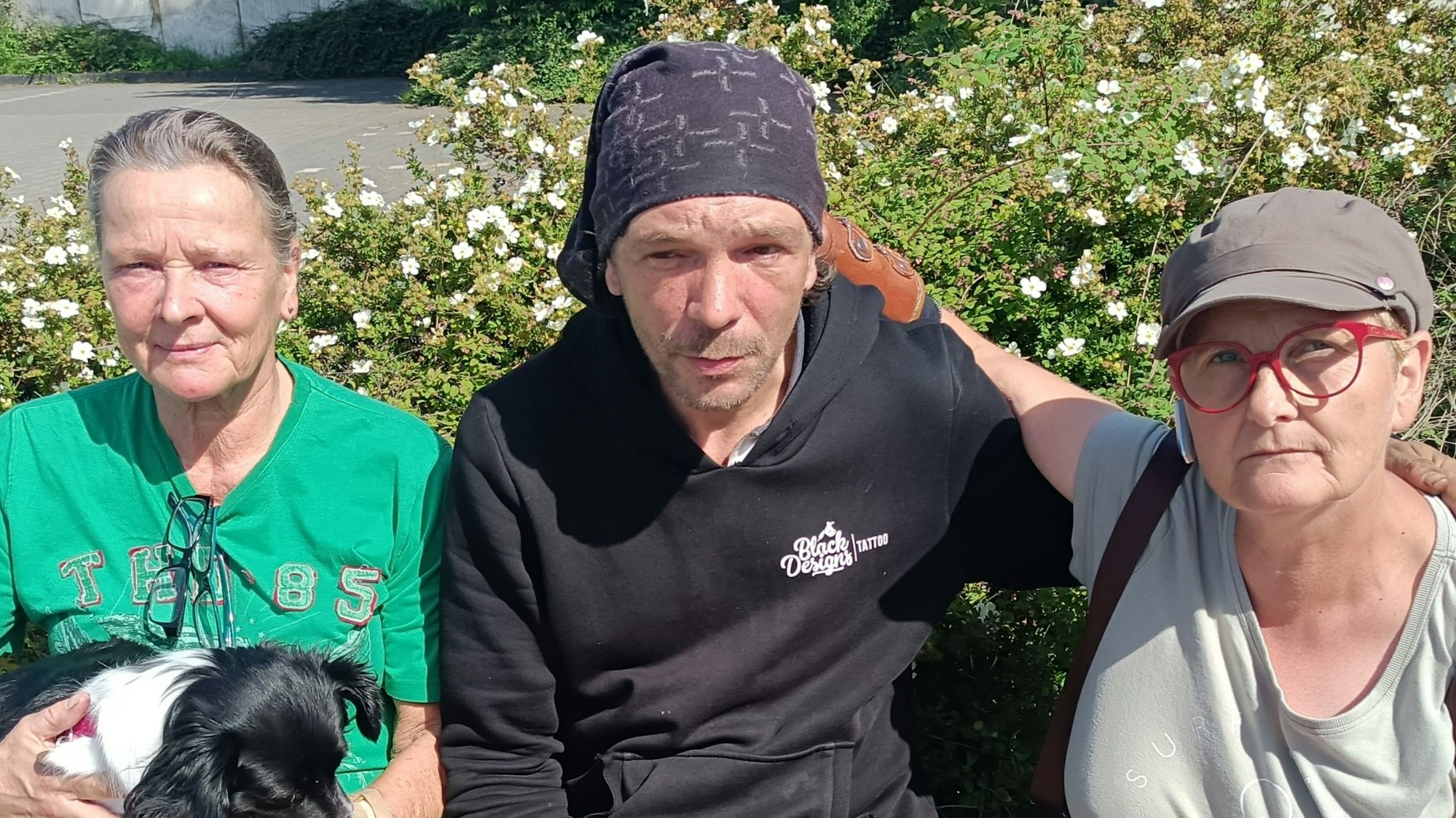 In der Mitte sitzt der Obdachlose Andreas Wüntenberg. Neben ihm sitzen zwei Frauen.