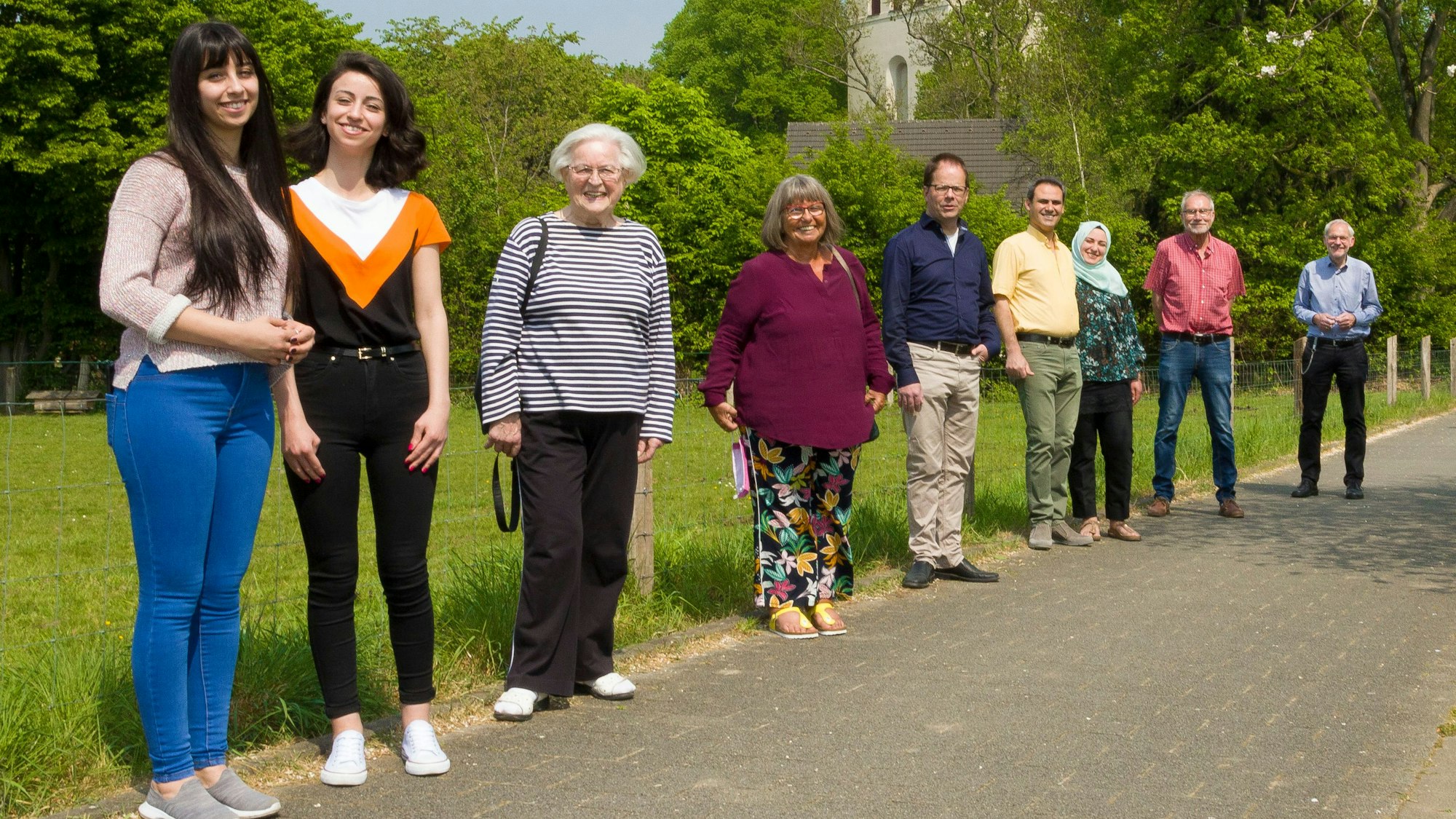 Shurook und Heba D. mit dem Mentoren-Team und Gemeindemitgliedern stehen auf der Wiese vor der Kirche St. Gereon.