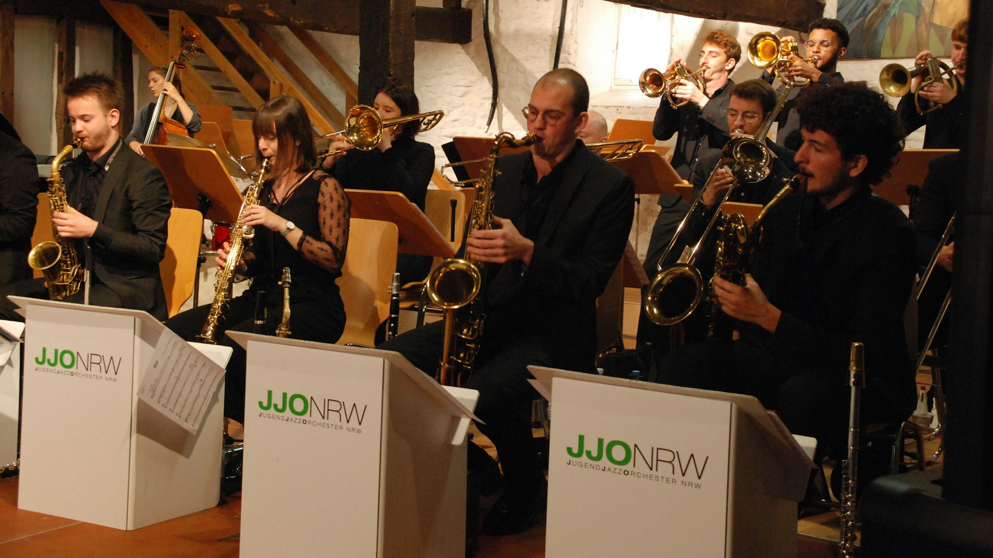 Mehrere Frauen und Männer sitzen an Notenpulten und spielen Instrumente.