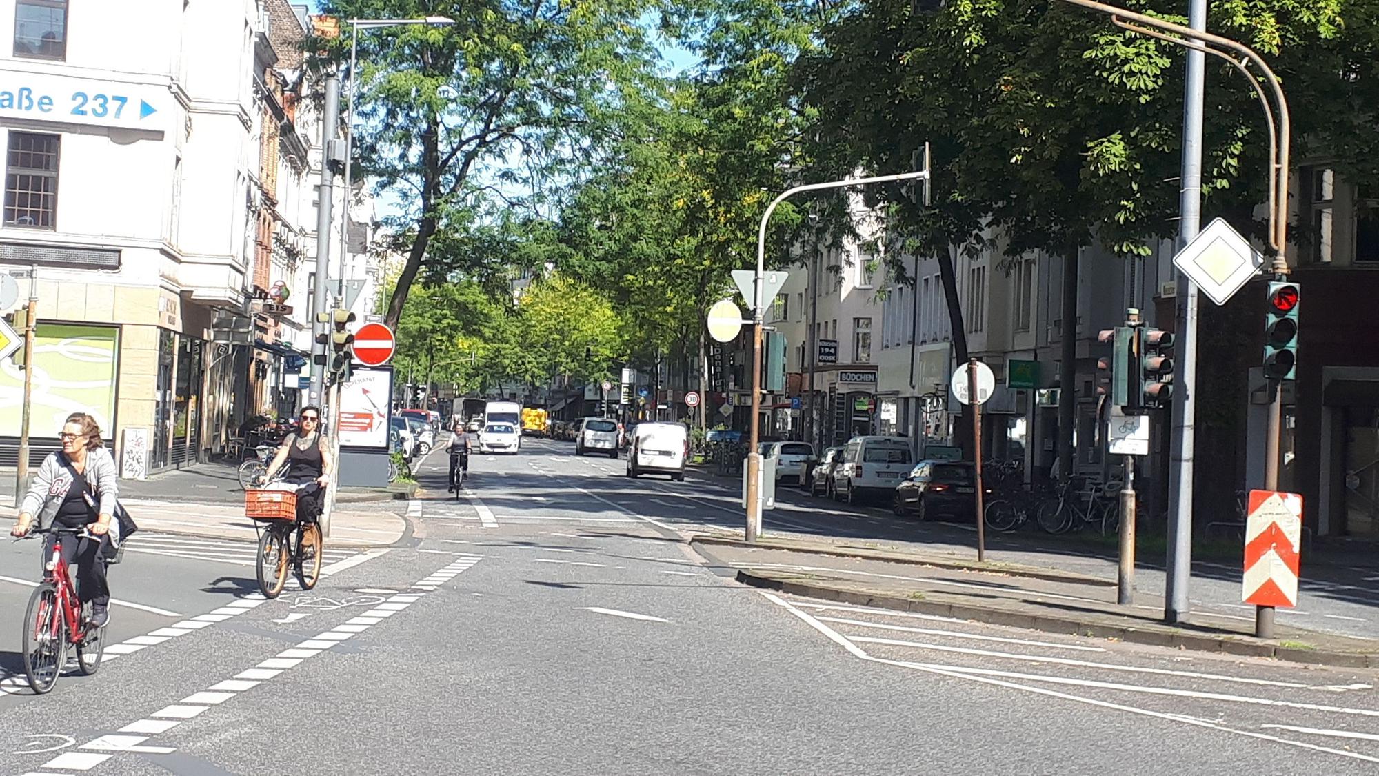 Die Kreuzung Neusser/Kempener/ Auerstraße ist zu sehen. Drei Straßen treffen aufeinander, Radfahrerinnen radeln über die Kreuzung.