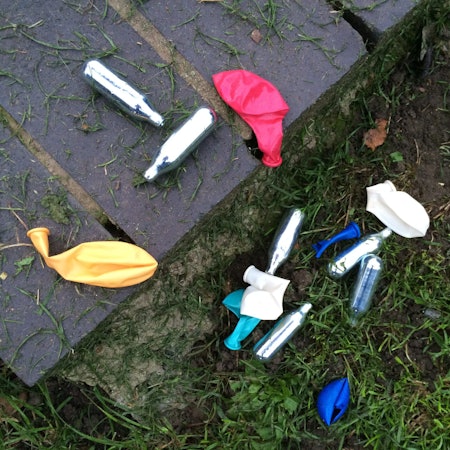 Lachgas-Kartuschen und Luftballons liegen in einem Park