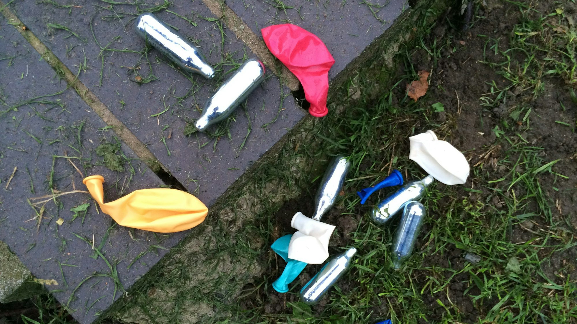 Lachgas-Kartuschen und Luftballons liegen in einem Park