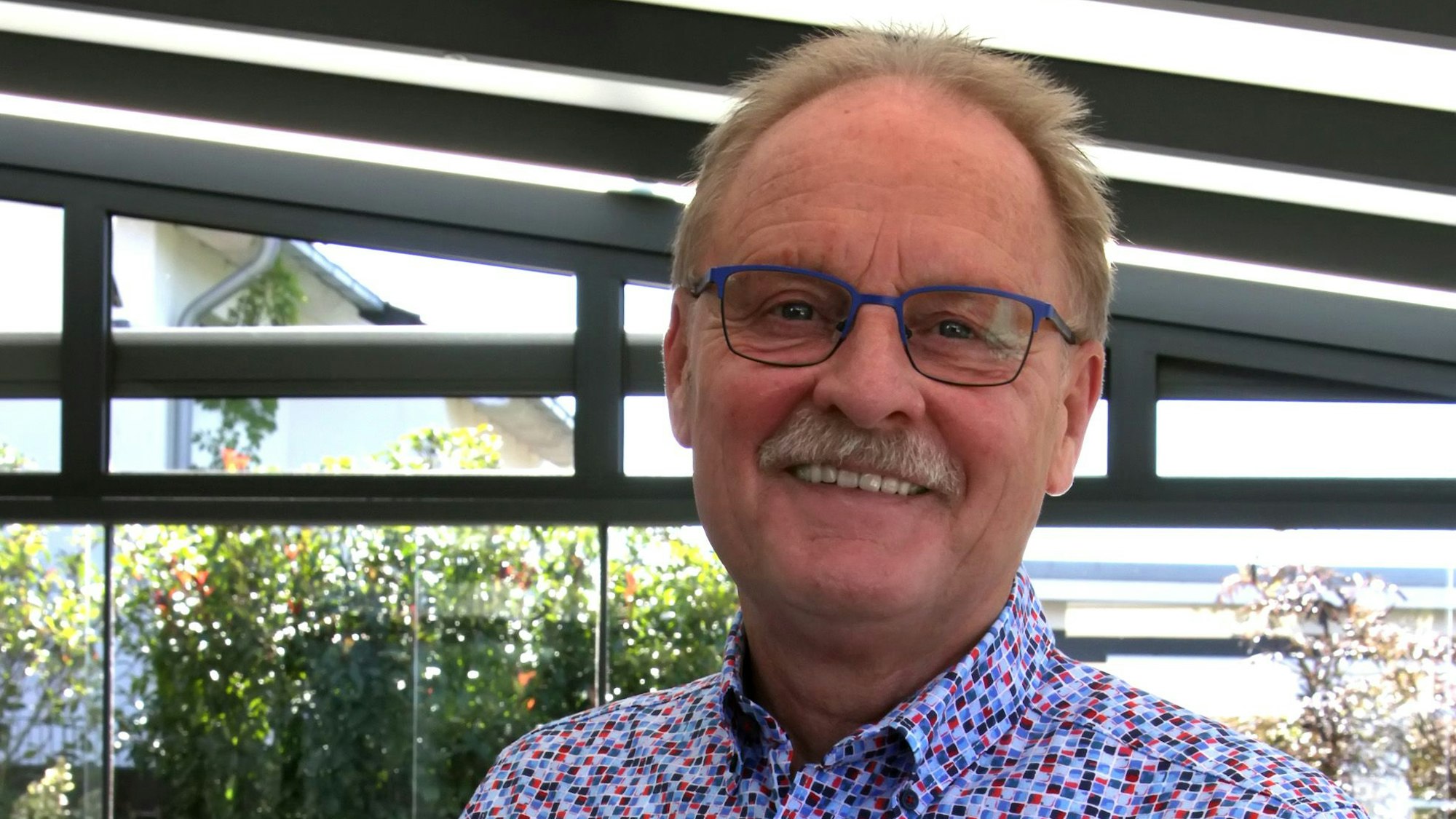 Ein Mann mit Brille und kleinteilig gemustertem Hemd.