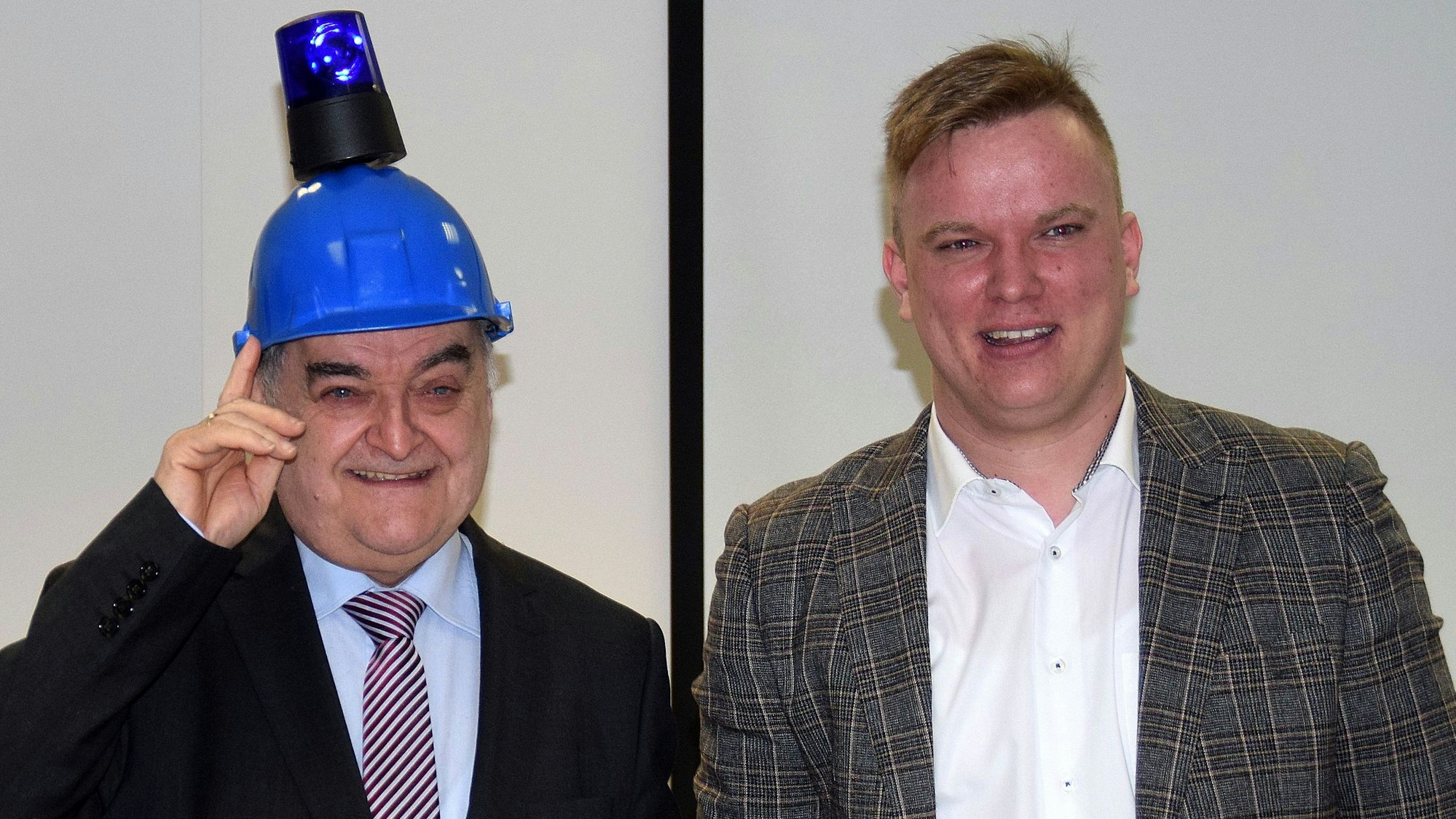 Herbert Reul hat einen blauen Helm mit einem Blaulicht auf dem Kopf. Neben ihm steht Dominik Pinsdorf.