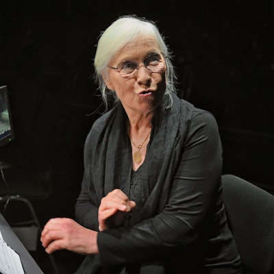 Beate Lenzen sitzt auf einem Stuhl und hat ein Heft vor sich liegen.