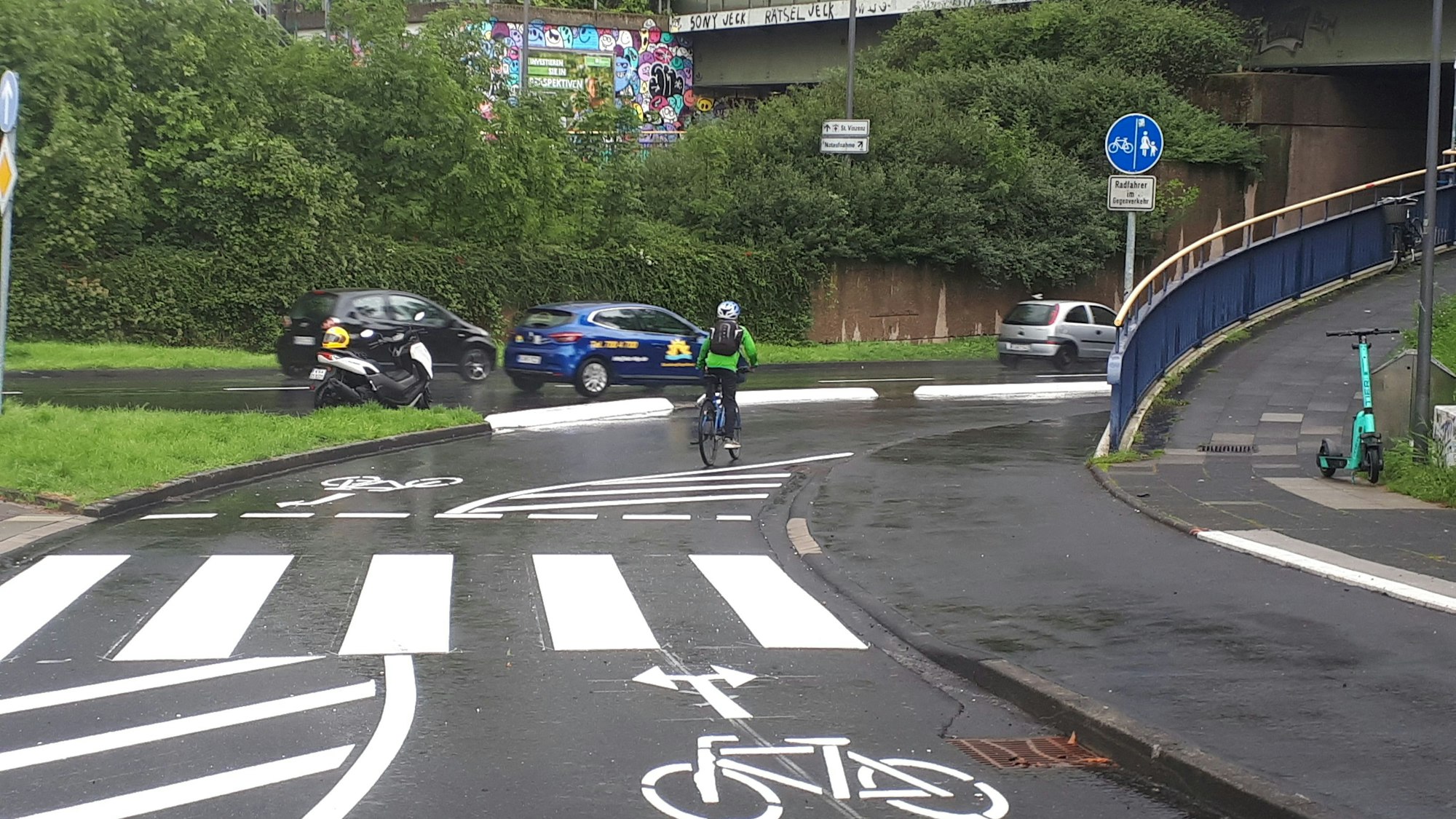 Ein Radfahrer fährt auf der einer Radspur an einer zweispurigen Straße. Es sind Fahrradpiktogramme mit Richtungspfeile und ein Zebrastreifen aufgemalt.