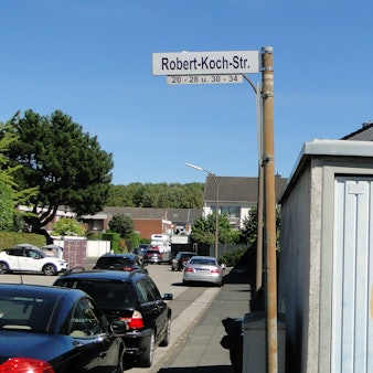 Ein Straßenschild mit der Aufschrift „Robert-Koch-Str.“ steht an einer Straßenecke.