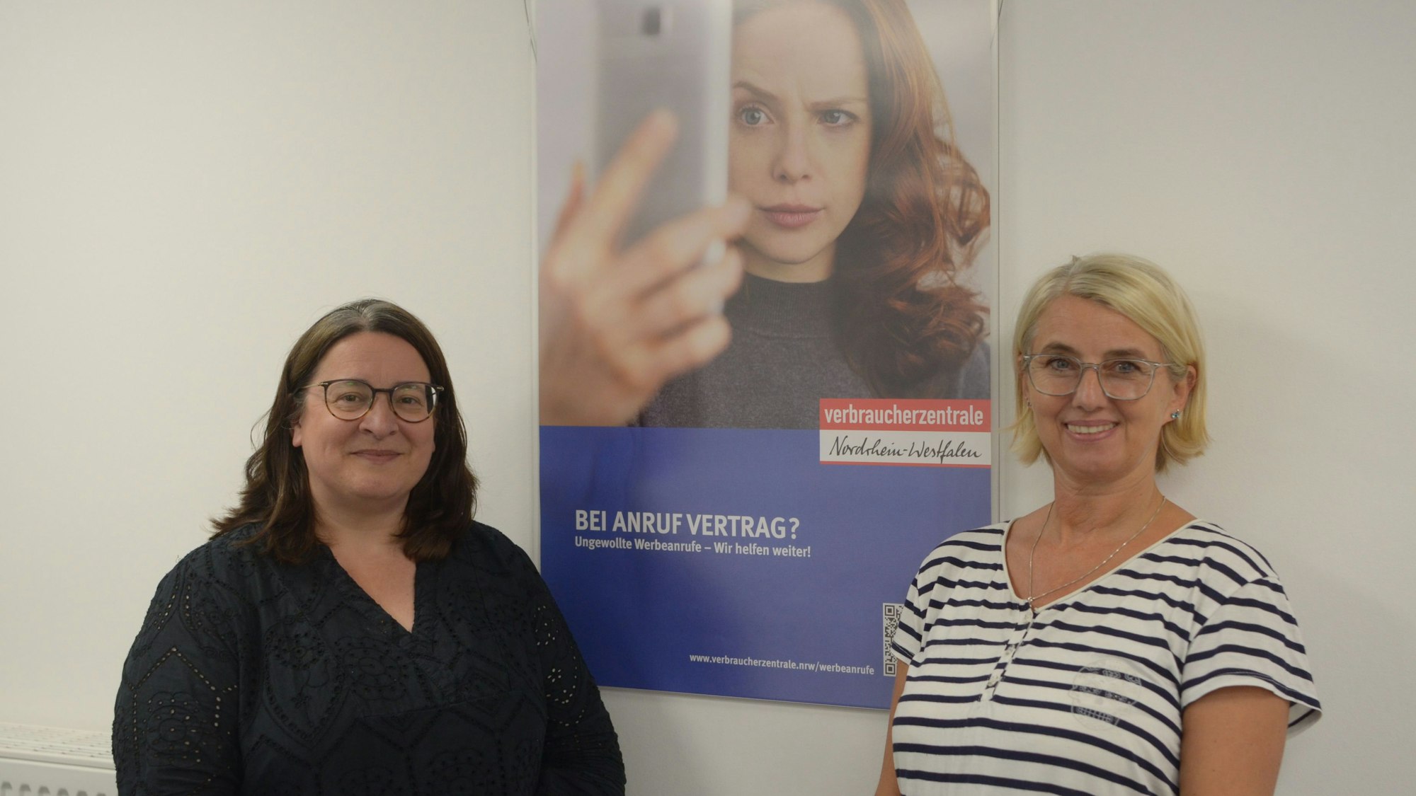 Die Leiterin der Verbraucherberatungsstelle Euskirchen, Monika Schiffer (l.), und Kriminalhauptkommissarin Eva Winkel stehen vor einem Plakat mit der Aufschrift „Bei Anruf Vertrag? Ungewollte Werbeanrufe – Wir helfen weiter!“