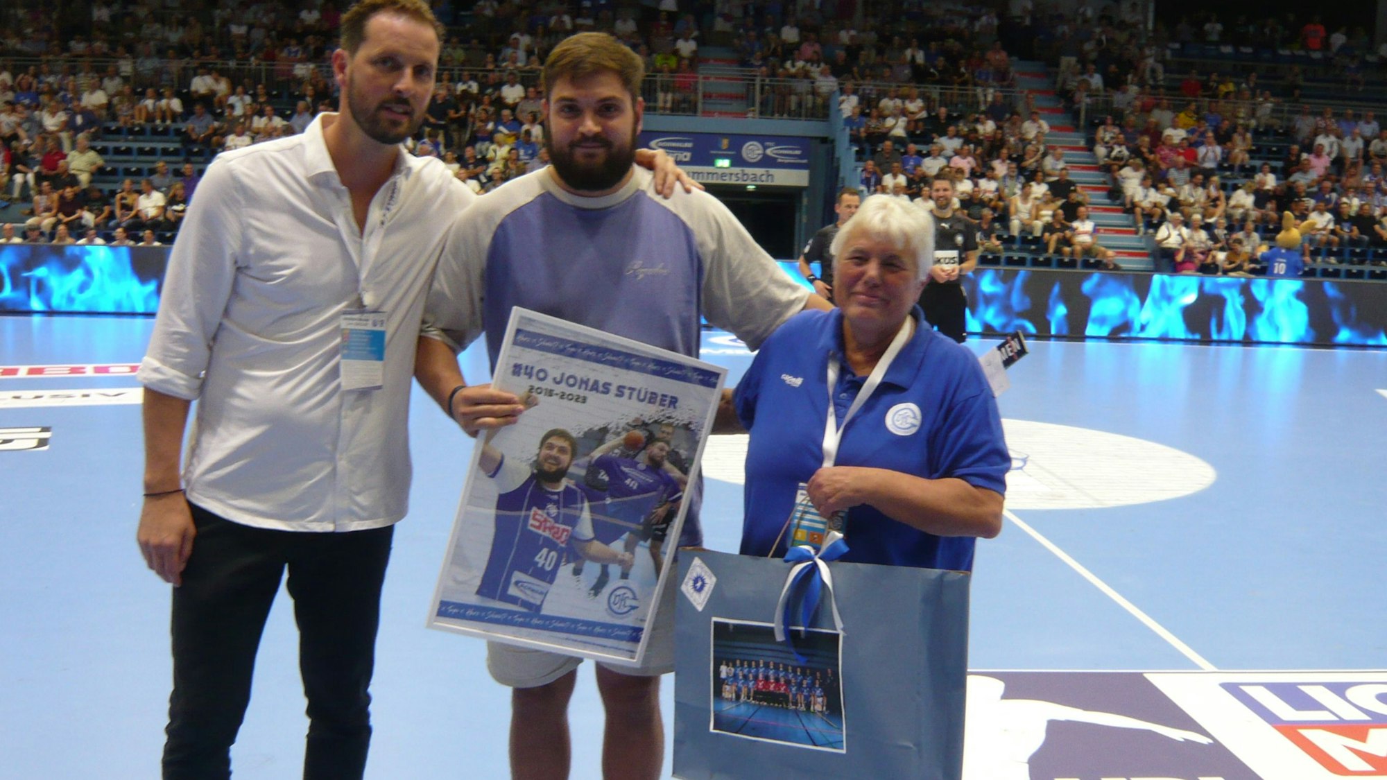 Der ehemalige Kreisläufer Jonas Stüber steht in der Mitte und hält die Geschenke in der Hand, die ihm VfL-Geschäftsführer Christoph Schindler (l.) und Claudia Thamm vom Fanclub Blue White Dynamite überreicht haben.