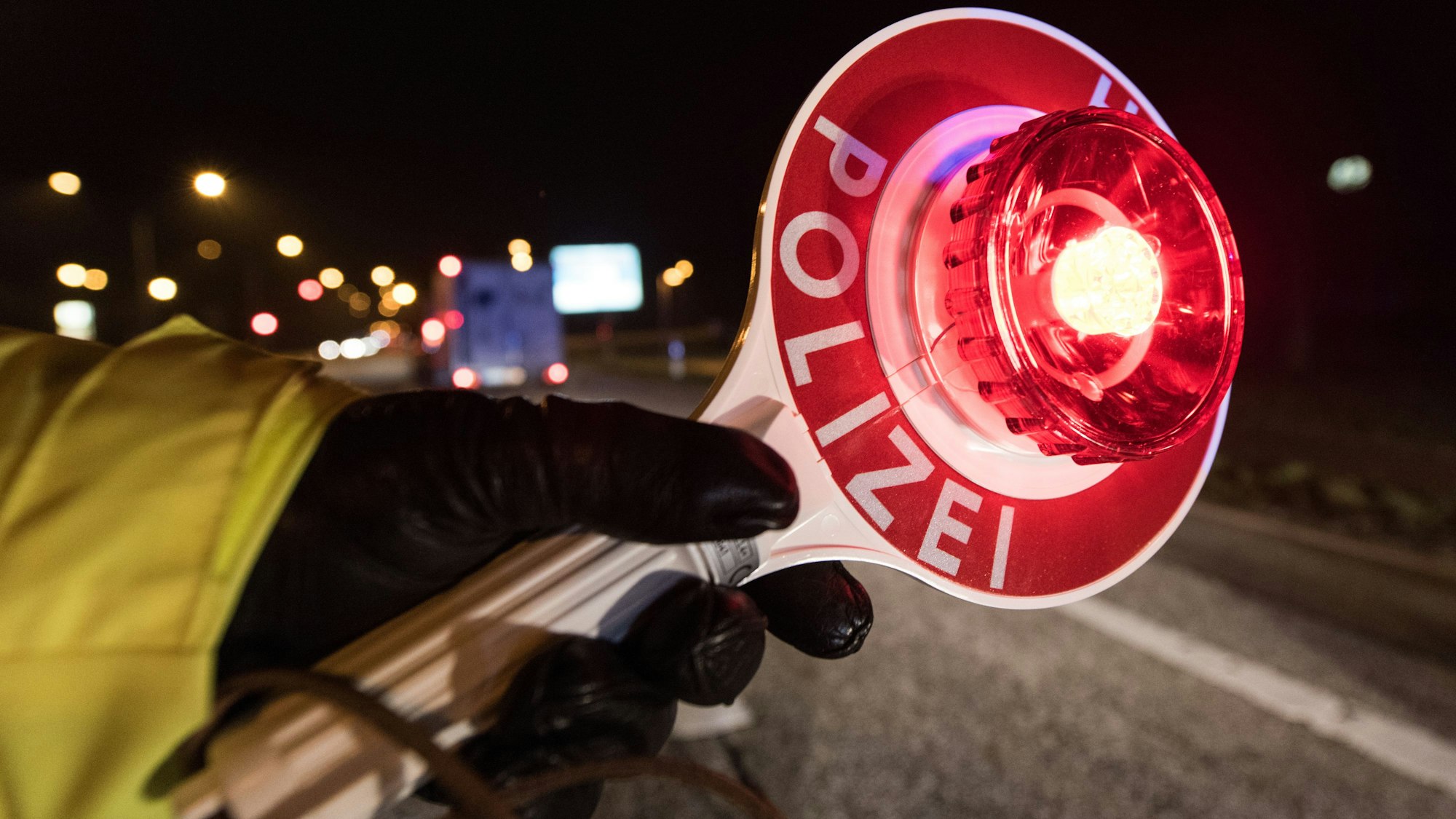 Ein Polizist hält während einer Verkehrskontrolle mit einer Haltekelle Fahrzeuge an.