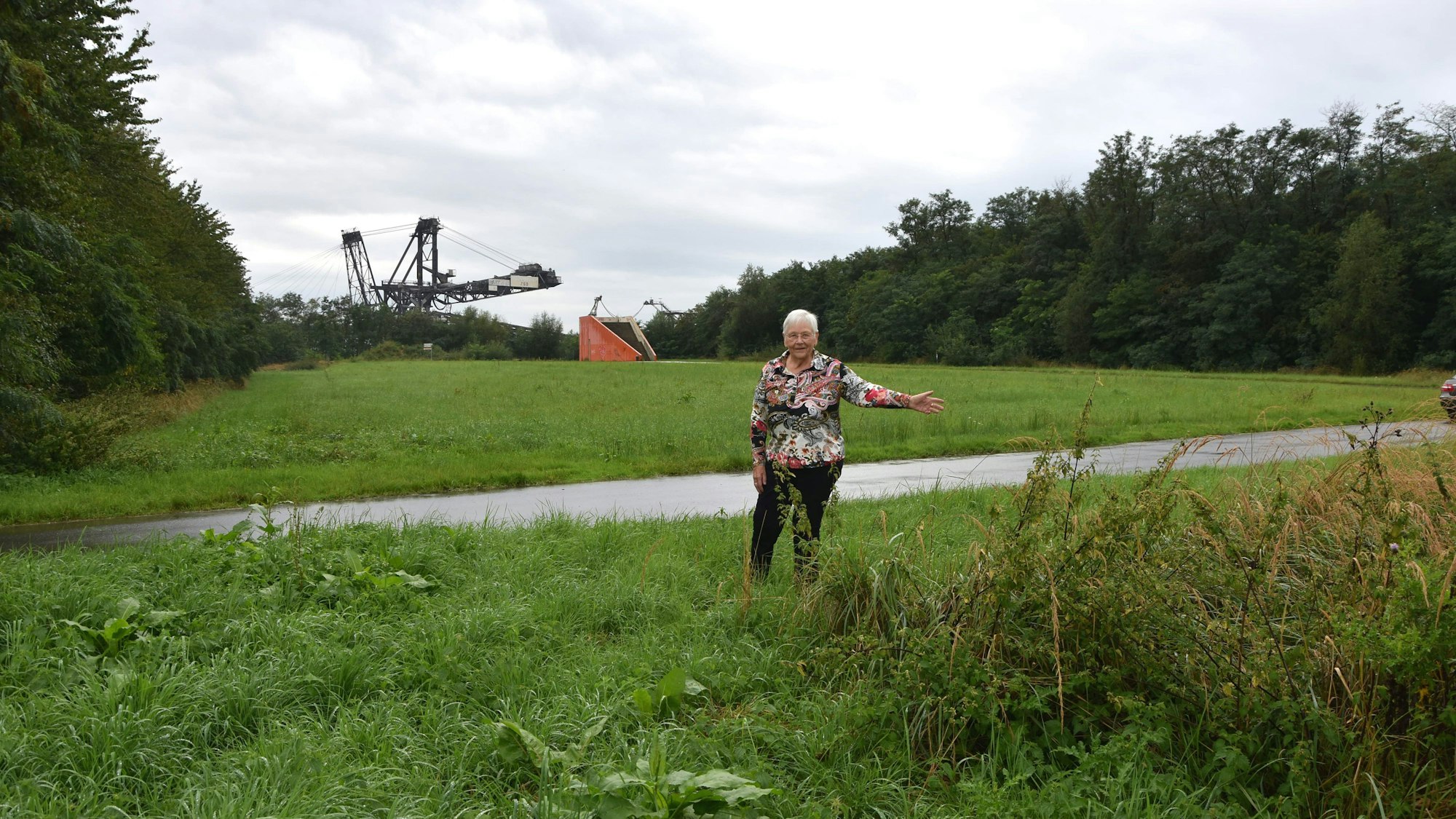 Eine Frau steht auf einer Gründfläche neben an einem Weg.