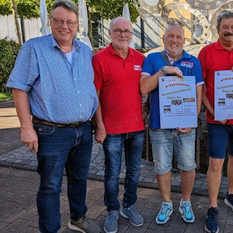 Vertreter der beiden Mechernicher Karnevalsvereine stehen in Sommerkleidung zusammen, drei Männer halten Plakate in der Hand.