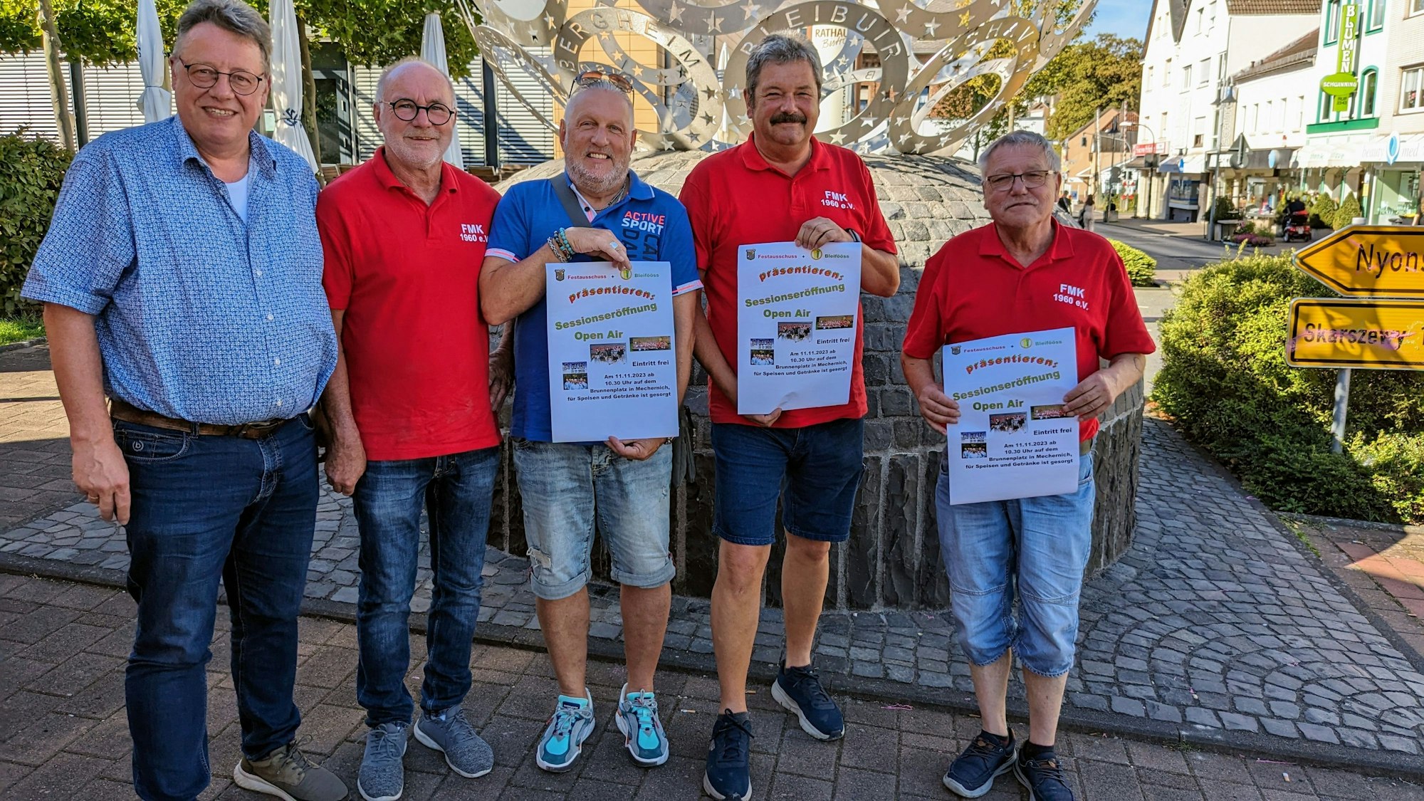 Vertreter der beiden Mechernicher Karnevalsvereine stehen in Sommerkleidung zusammen, drei Männer halten Plakate in der Hand.