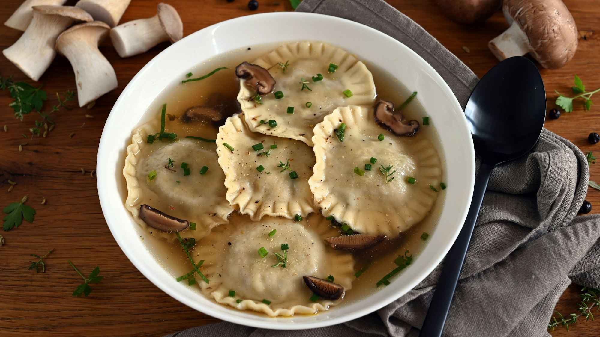 In einem Suppenteller schwimmen Ravioli und Pilze in einer Flüssigkeit.