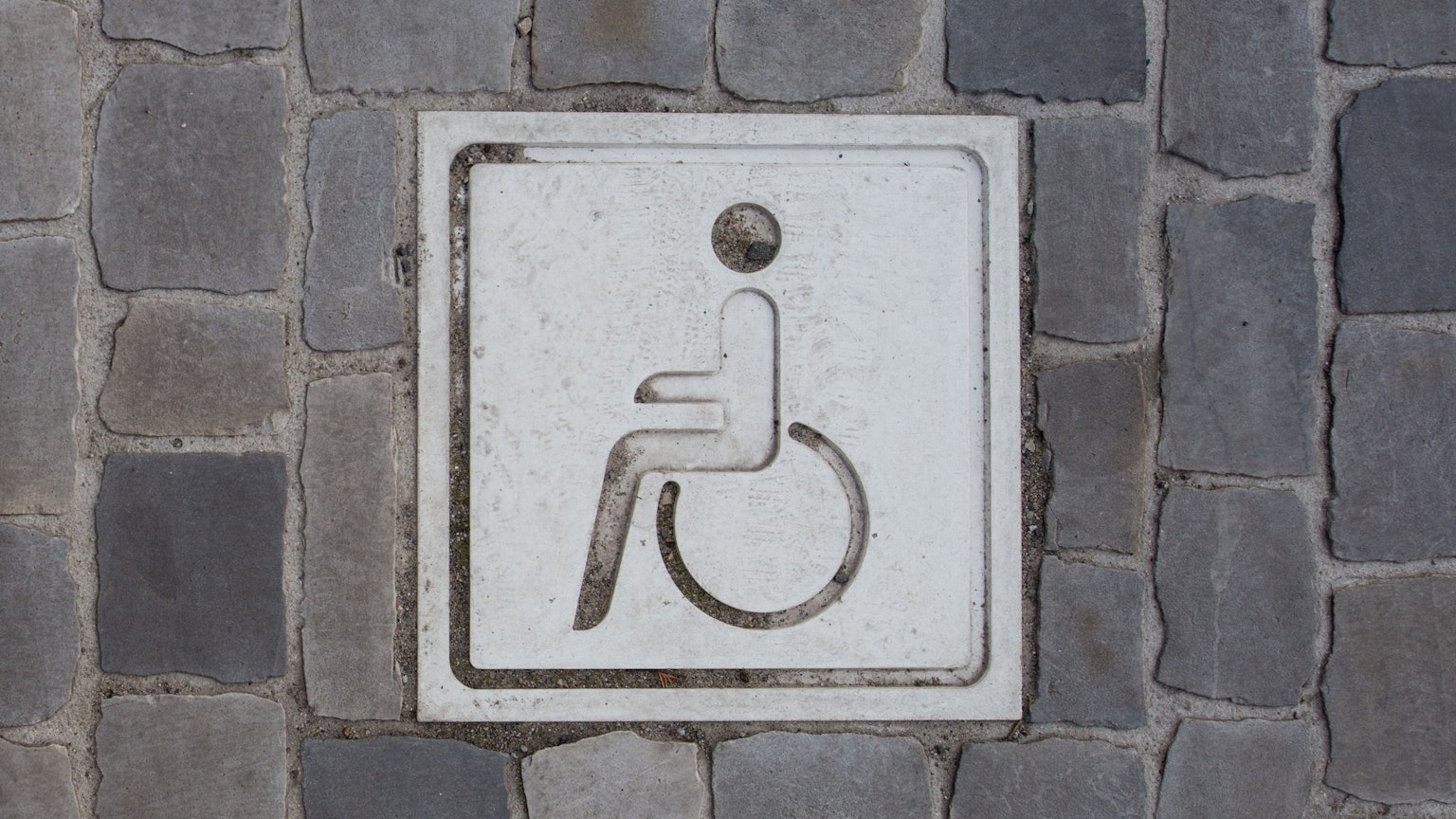 Auf einem Boden aus Pflastersteinen ist ein Piktogramm von einer Person in einem Rollstuhl.
