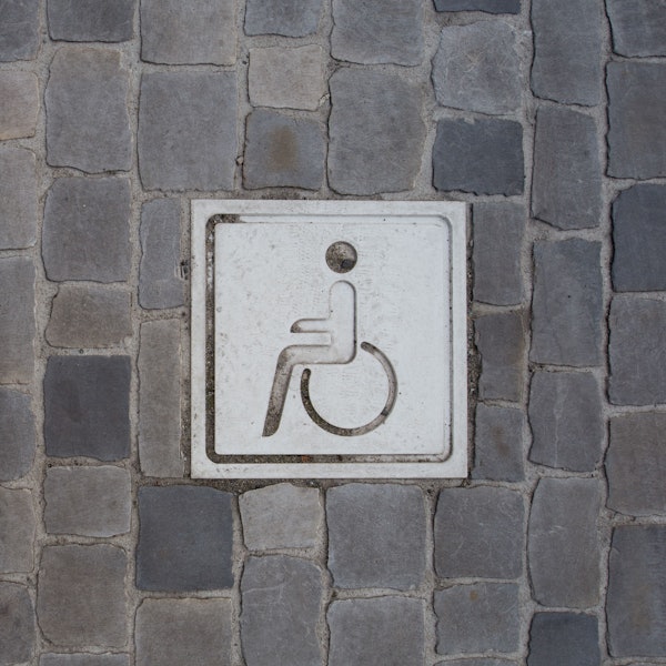 Auf einem Boden aus Pflastersteinen ist ein Piktogramm von einer Person in einem Rollstuhl.
