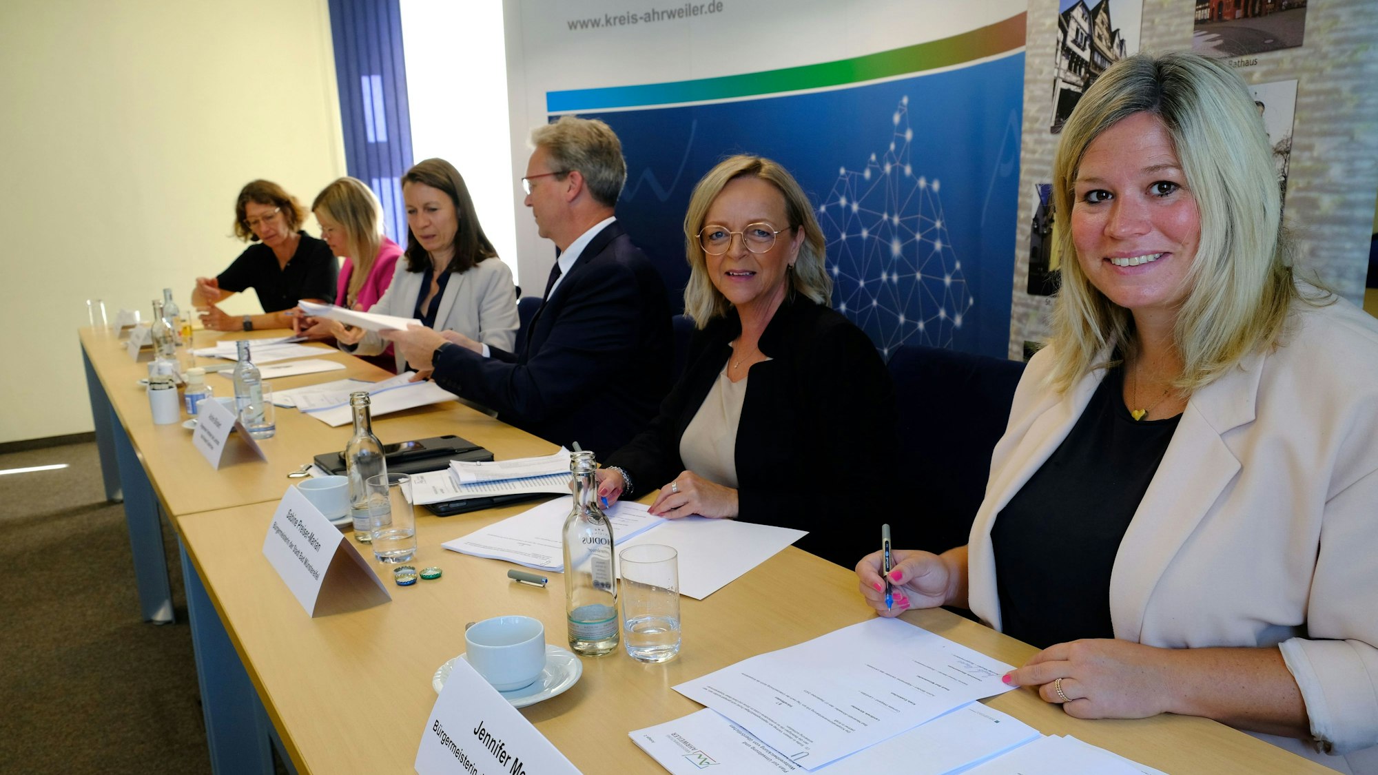 Das Bild zeigt Jennifer Meuren, Sabine Preiser-Marian und Achim Blindert (v. r.) beim Unterzeichnen eines Papiers. Im Hintergrund sind die Landrätinnen Cornelia Weigand (Ahrweiler) und Julia Gieseking (Vulkaneifel) zu erkennen.