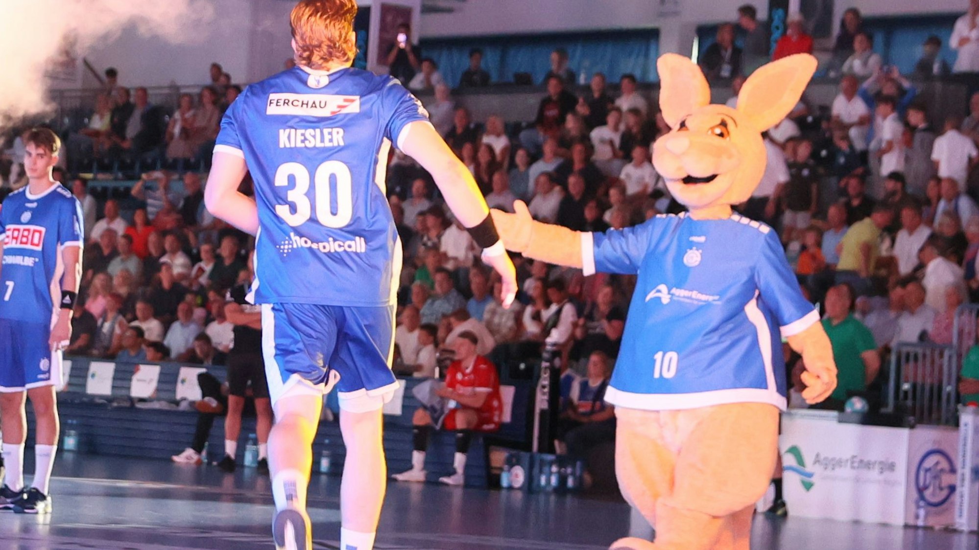 VfL-Handballer Tom Kiesler läuft in die Schwalbe-Arena und klatscht Maskottchen Gummi ab.
