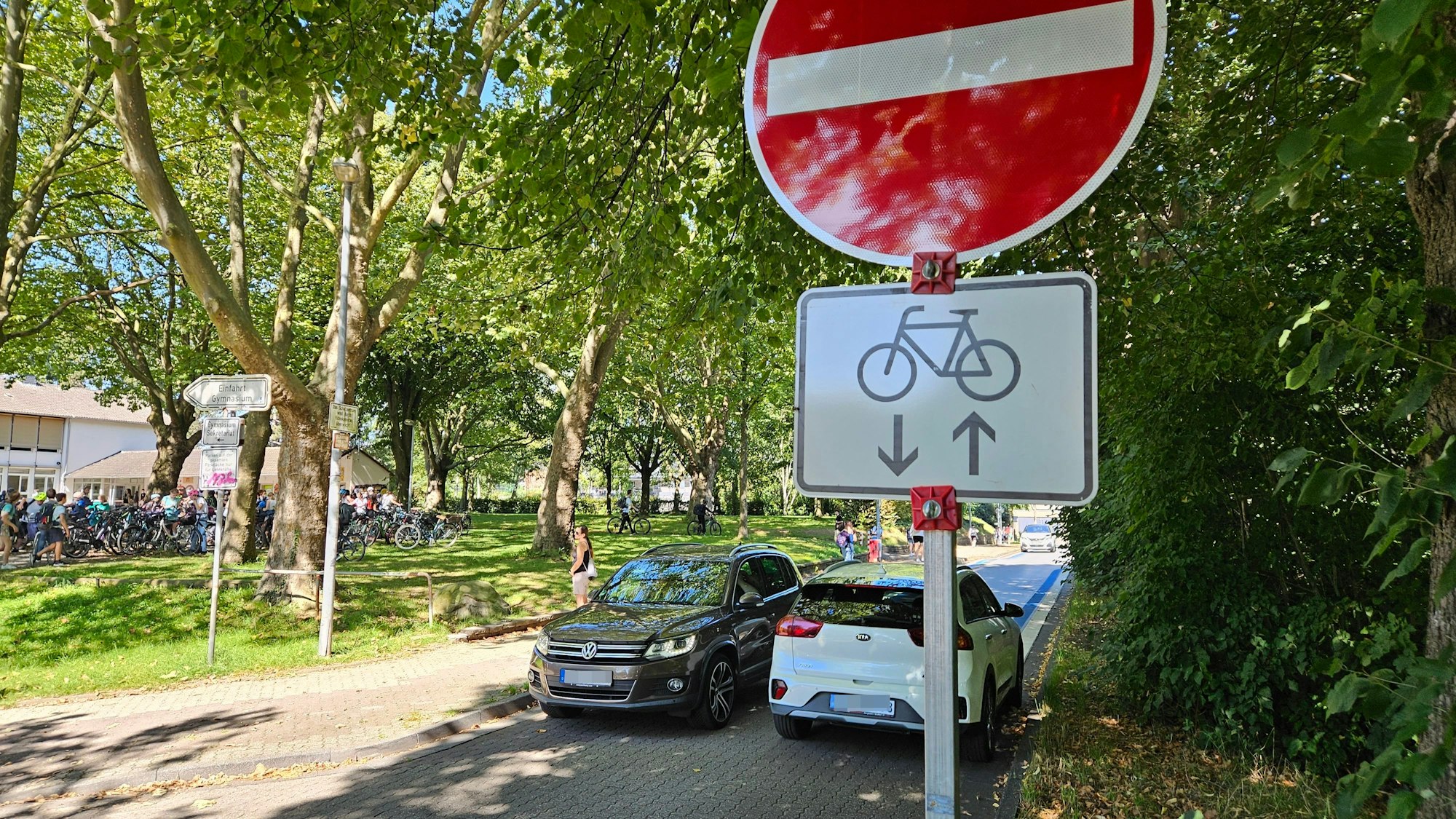 Zwei Autos fahren auf einer Straße in unterschiedliche Richtungen, ein Schild zeigt an, dass für eines der Autos die Durchfahrt verboten ist.