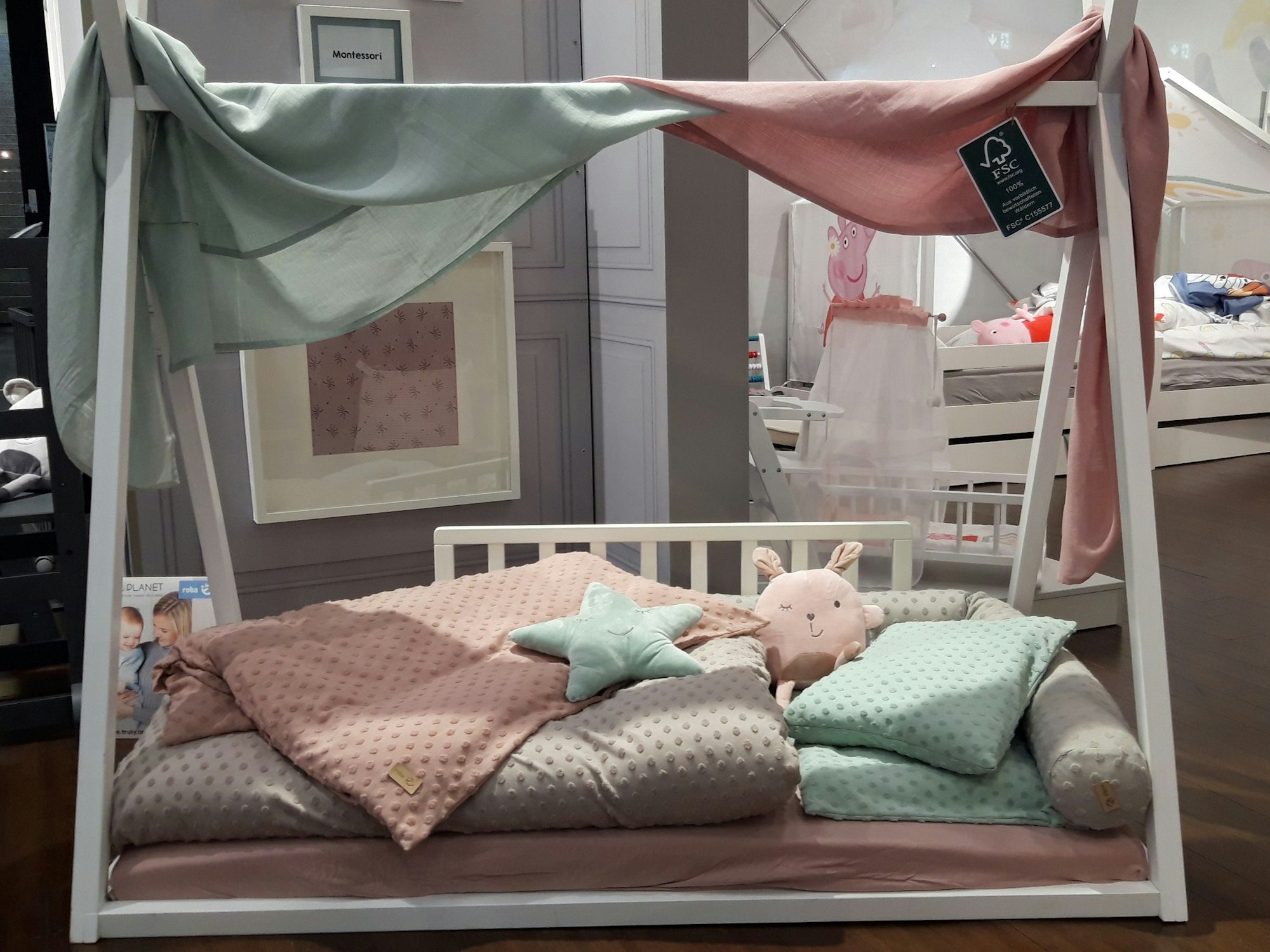 Kinderbett mit zeltartigem Überbau, Kissen und Decken in Grau, Altrosa und Hellgrün.