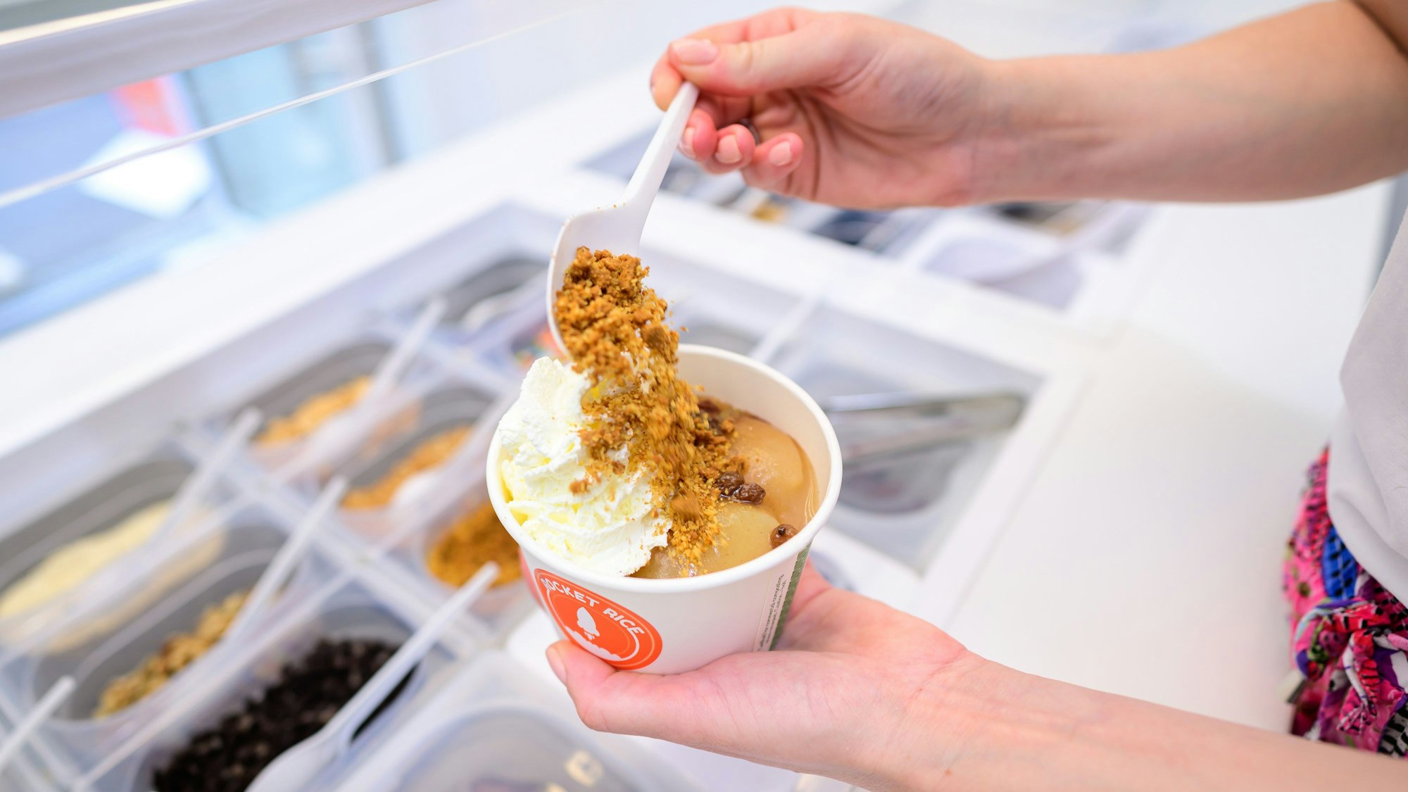 Eine Hand befüllt eine Schale Milchreis mit Toppings.