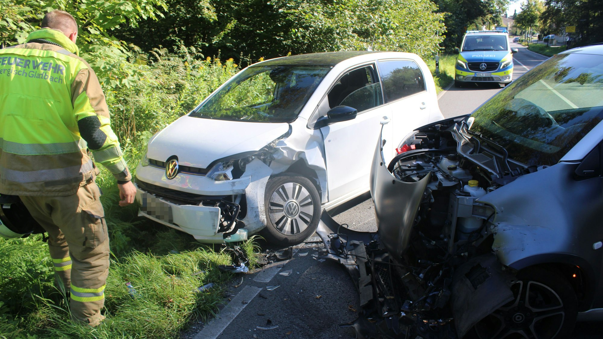 Zwei schwer beschädigte Fahrzeuge stehen auf und neben einer Straße in Bergisch Gladbach.